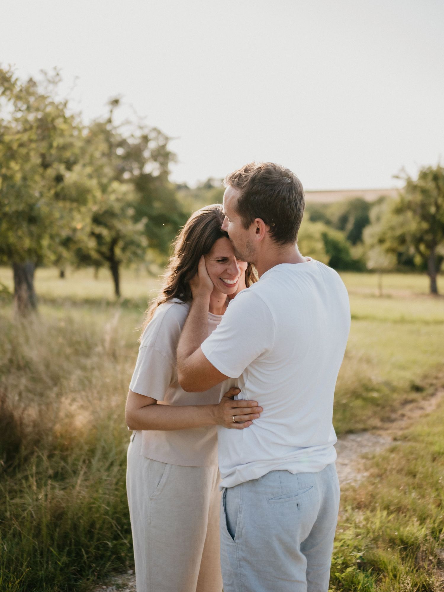 A couple shares intimate moments in a sun-drenched field during a romantic outdoor photoshoot.