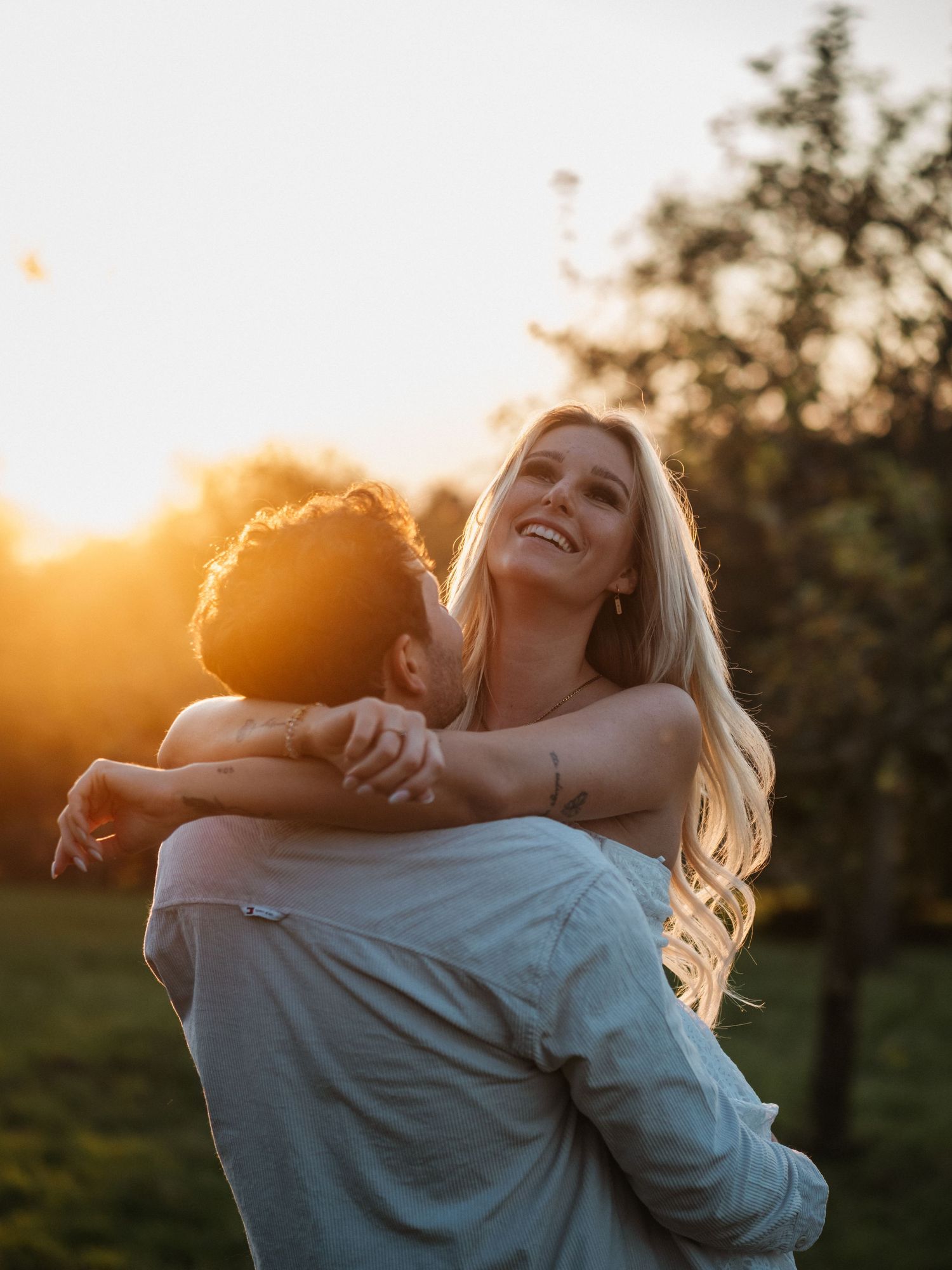 Two people embrace and laugh together in a joyful moment during golden sunset in a grassy field.