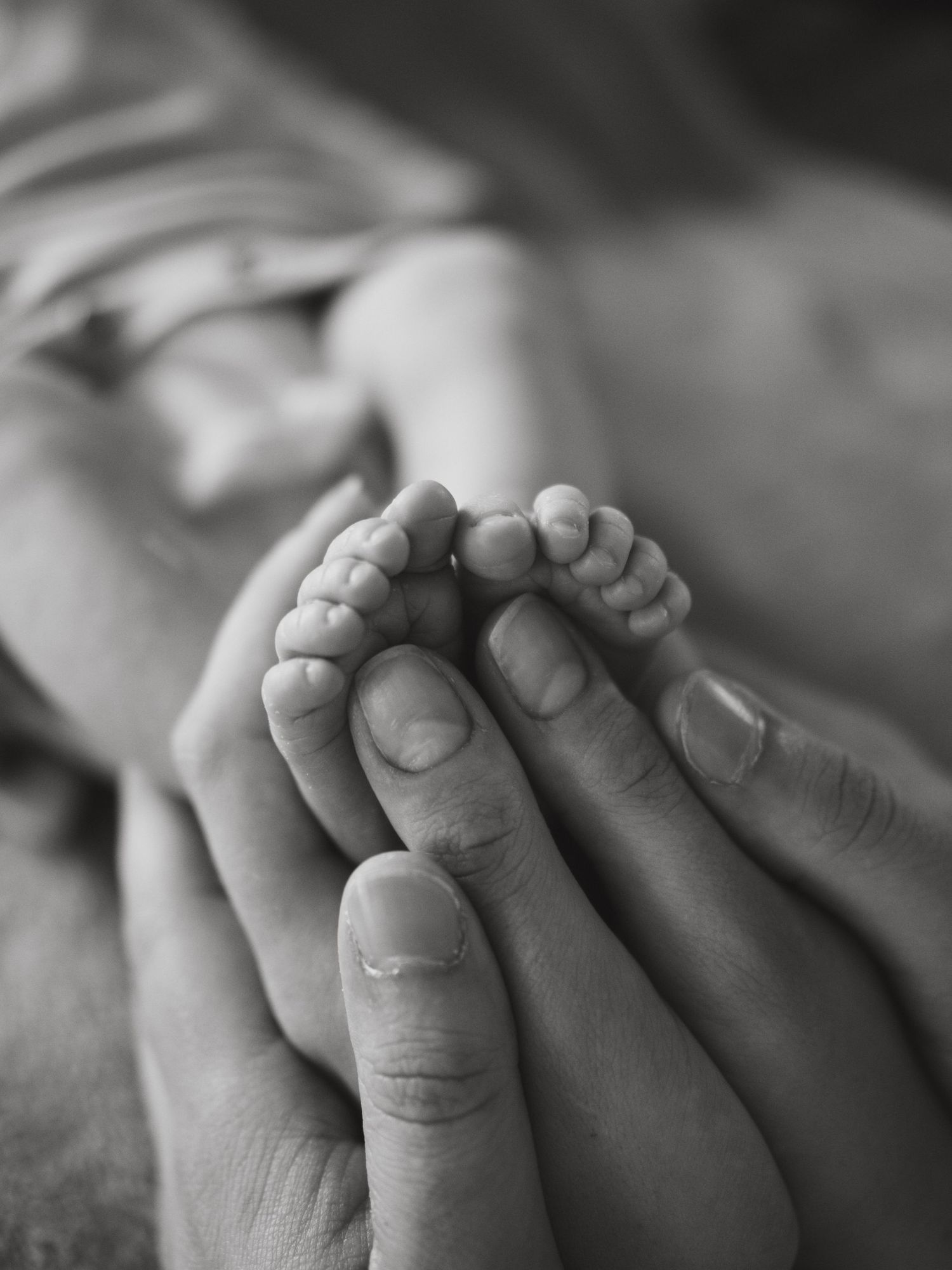 Black and white close-up photograph of tiny baby toes being gently held by adult hands.