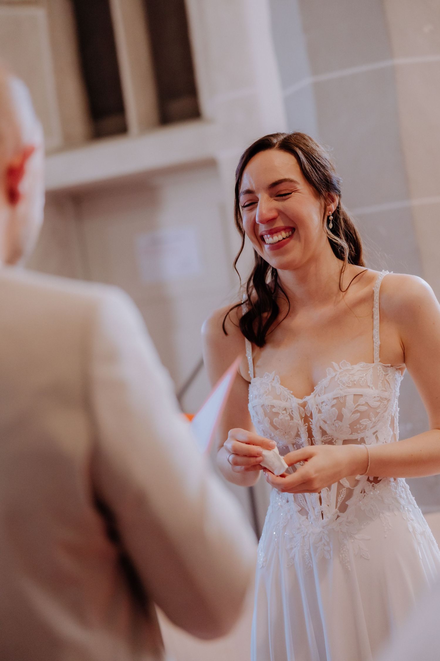 Bride in lace wedding dress laughing joyfully during ring exchange ceremony.
