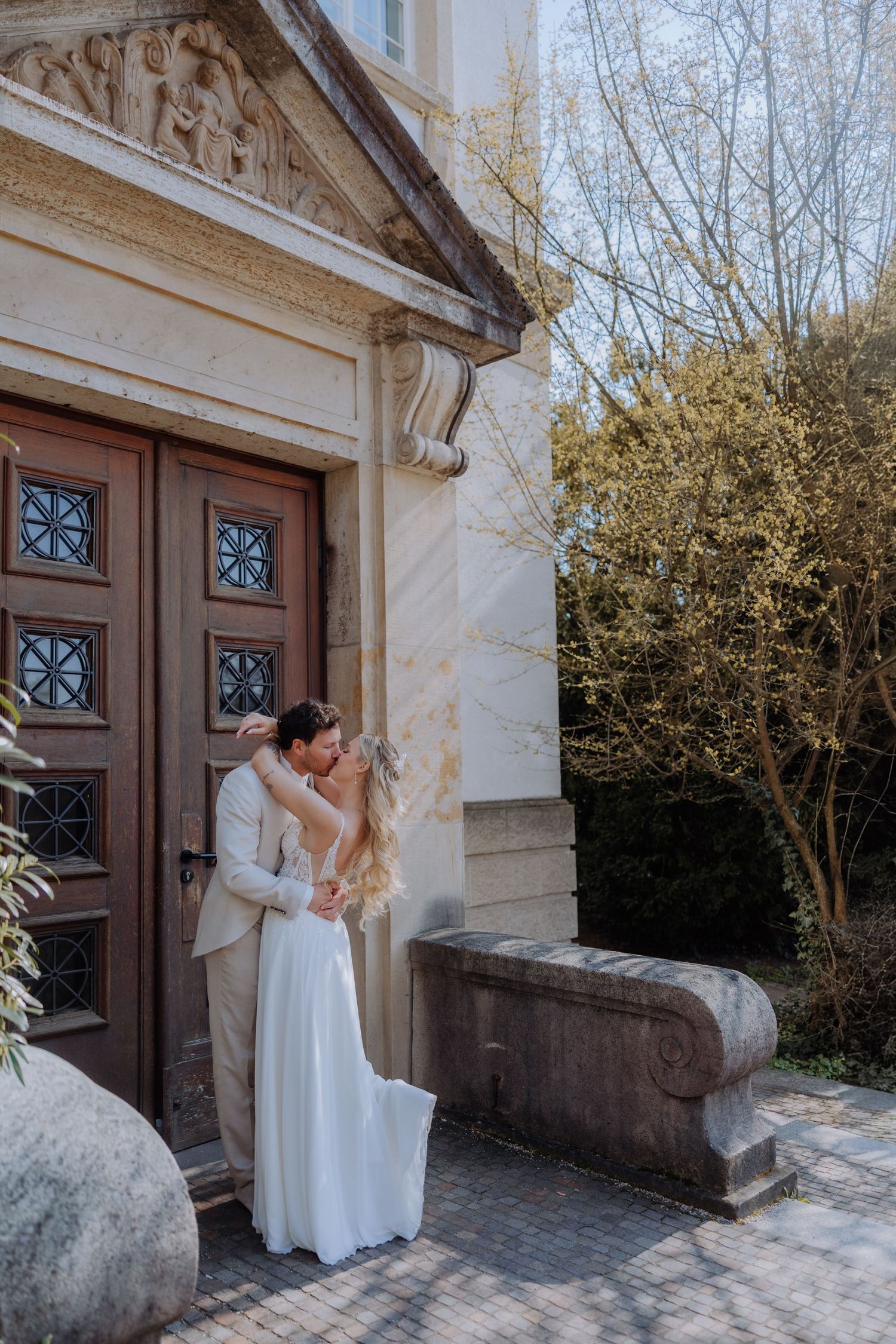 Bride and groom sharing a romantic kiss in front of an elegant building entrance on their wedding day.