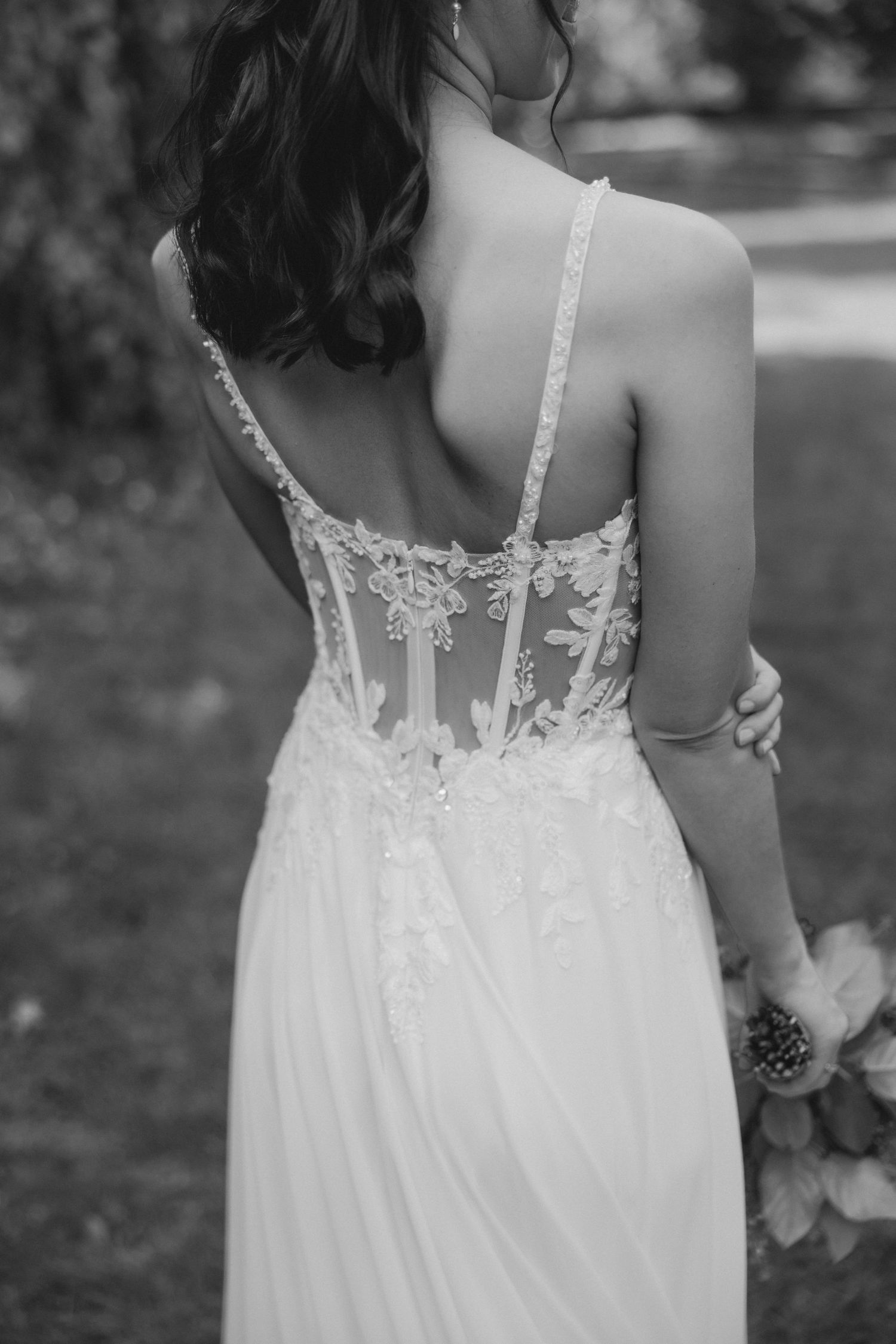 Black and white photo of a bride in a backless lace wedding gown with floral embroidery and spaghetti straps.