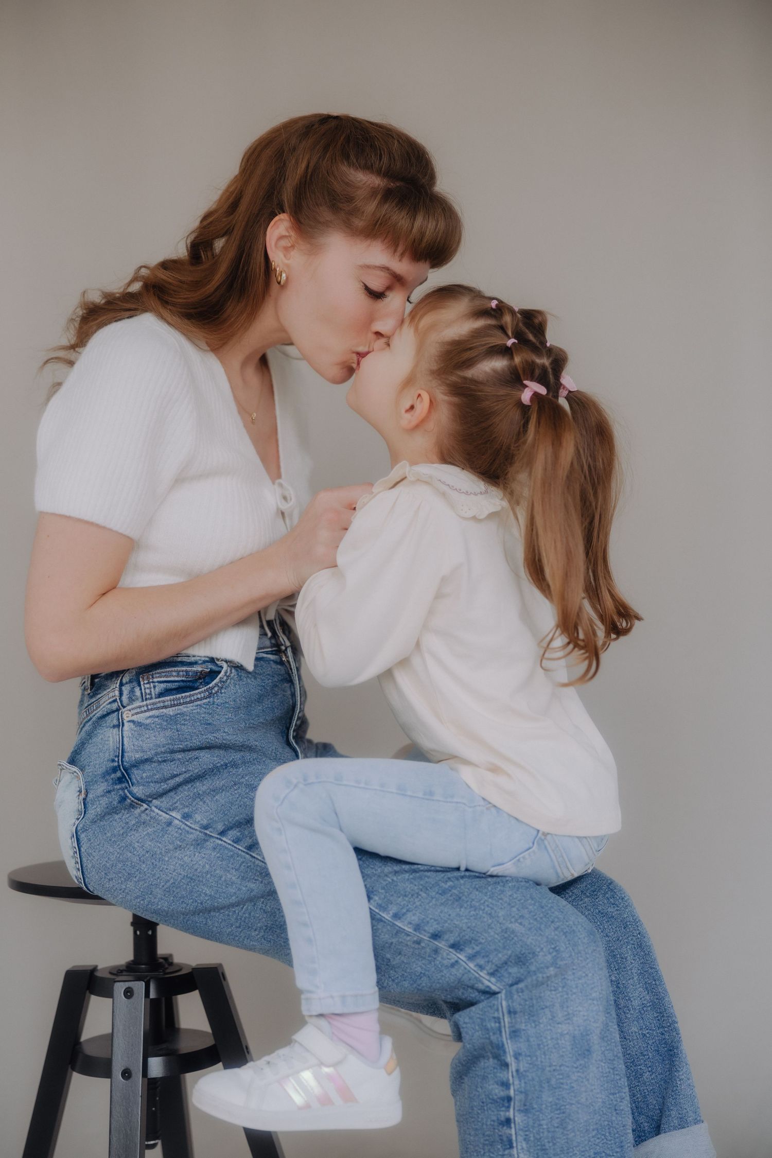 Sweet candid moments between a parent and child sitting on a stool in matching white shirts and denim.