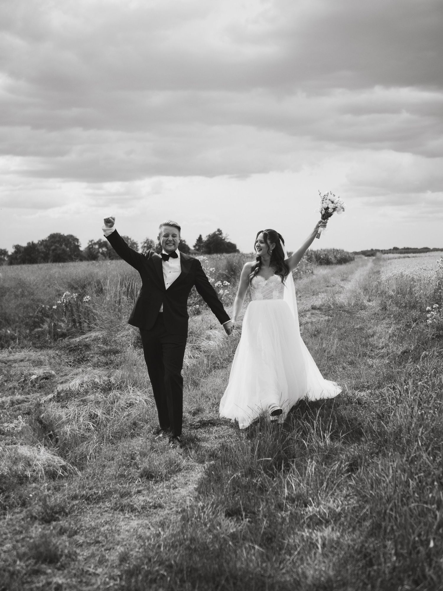 Joyful newlyweds celebrate in a dramatic black and white photo series in an open field.