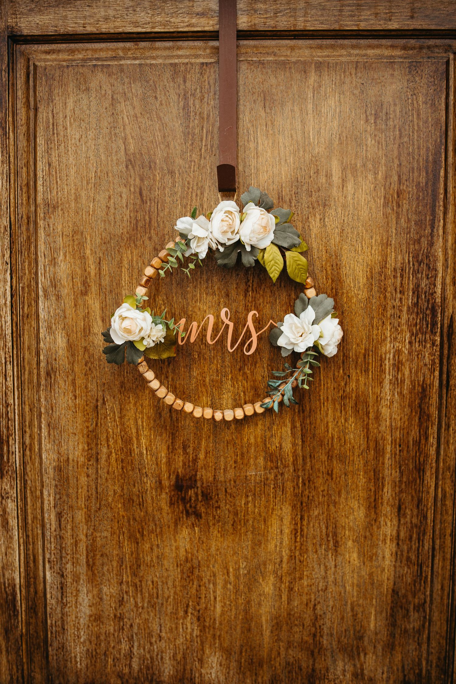 Decorative wooden wedding wreath with white roses and 'mrs' text hanging on vintage door.