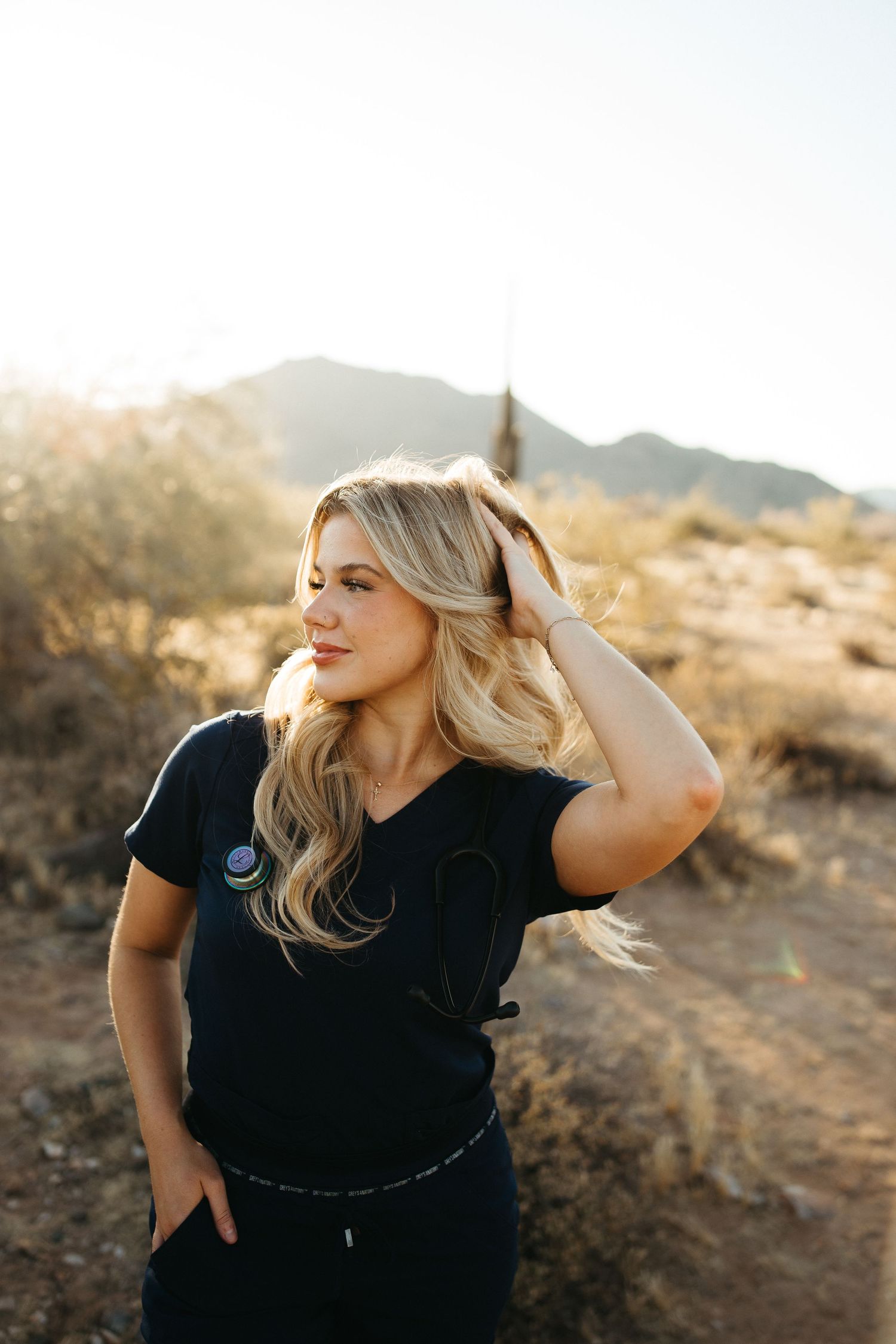 Person in black outfit poses against desert landscape during sunset.