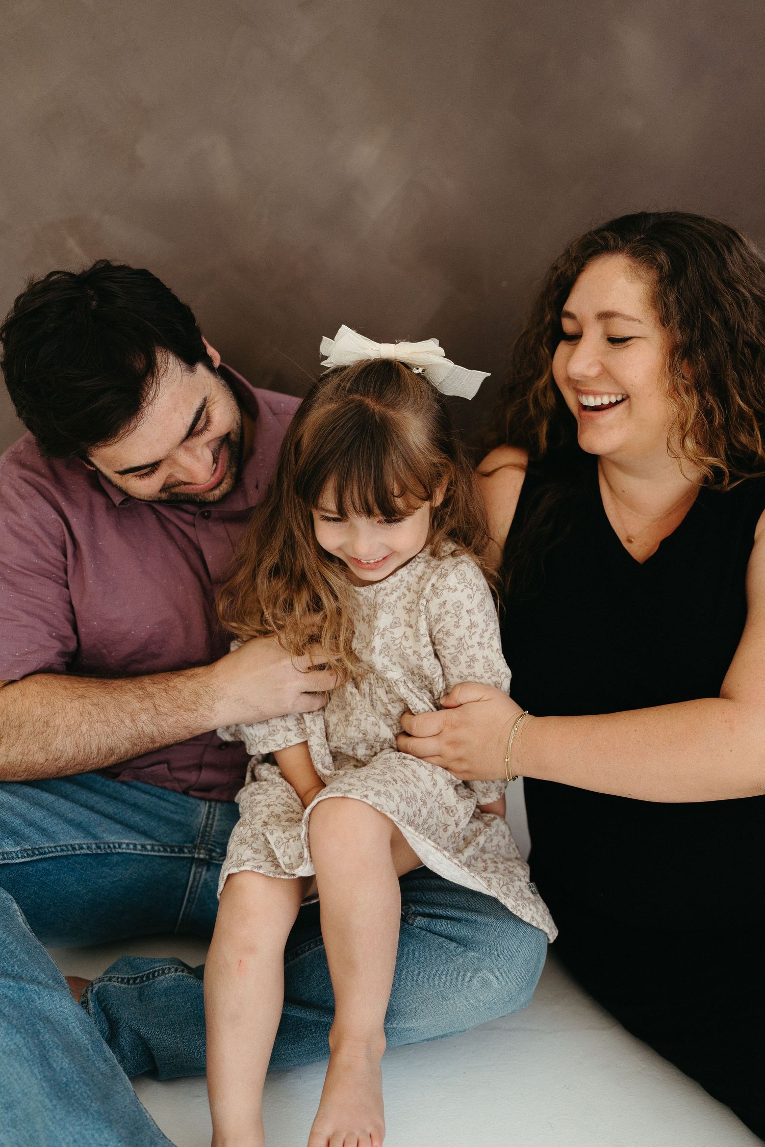 A playful family photography session capturing candid laughter and intimate moments against a dark studio backdrop.