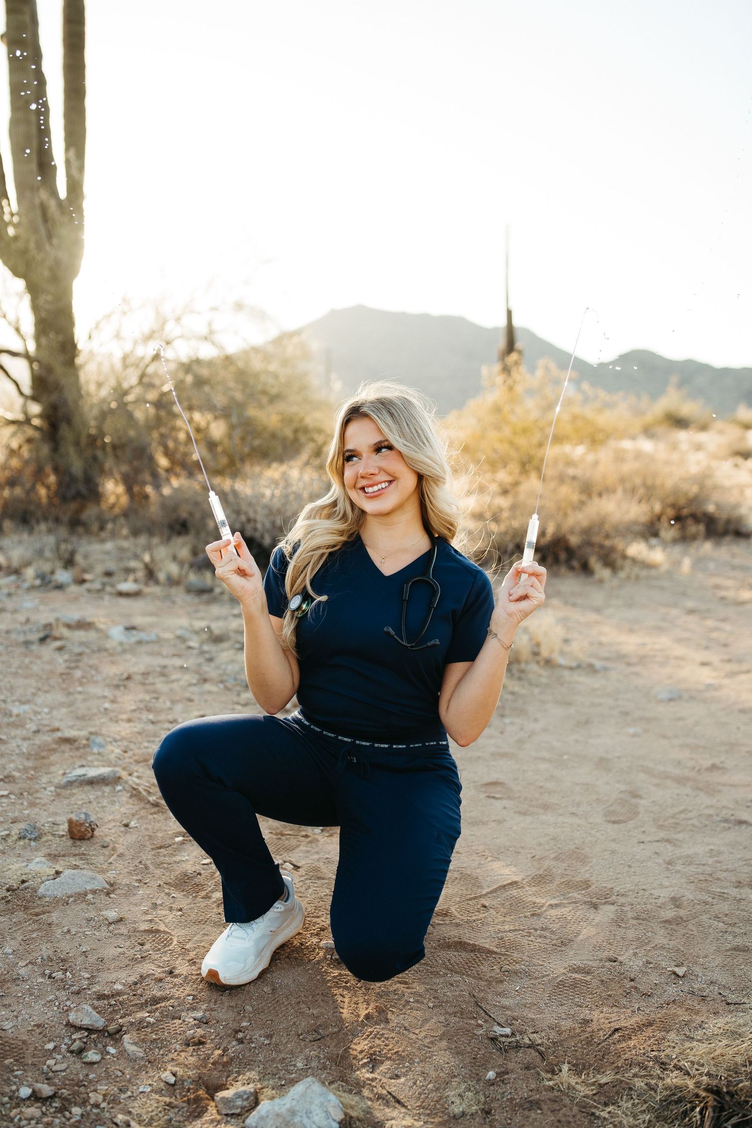 A person poses in casual navy attire near a saguaro cactus in a desert landscape at sunset.