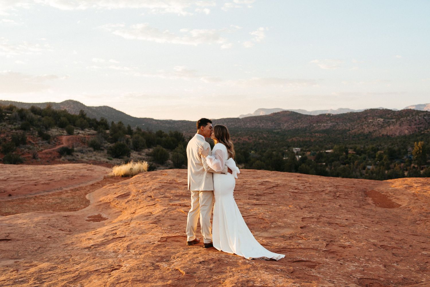 Wedding couple standing on red rocks during sunset in desert landscape.