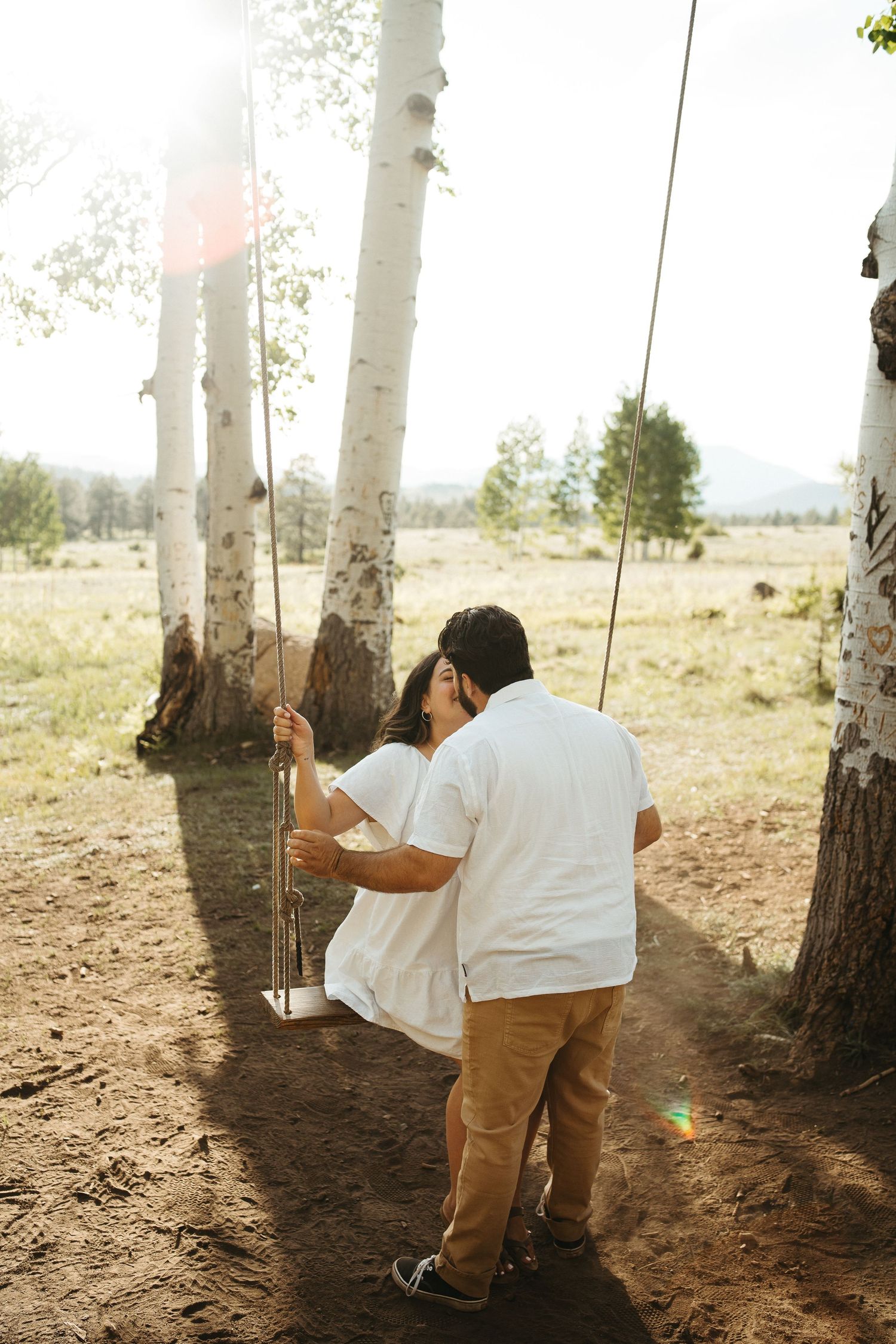 Romantic moment on tree swing among white birch trees in sunlit meadow.