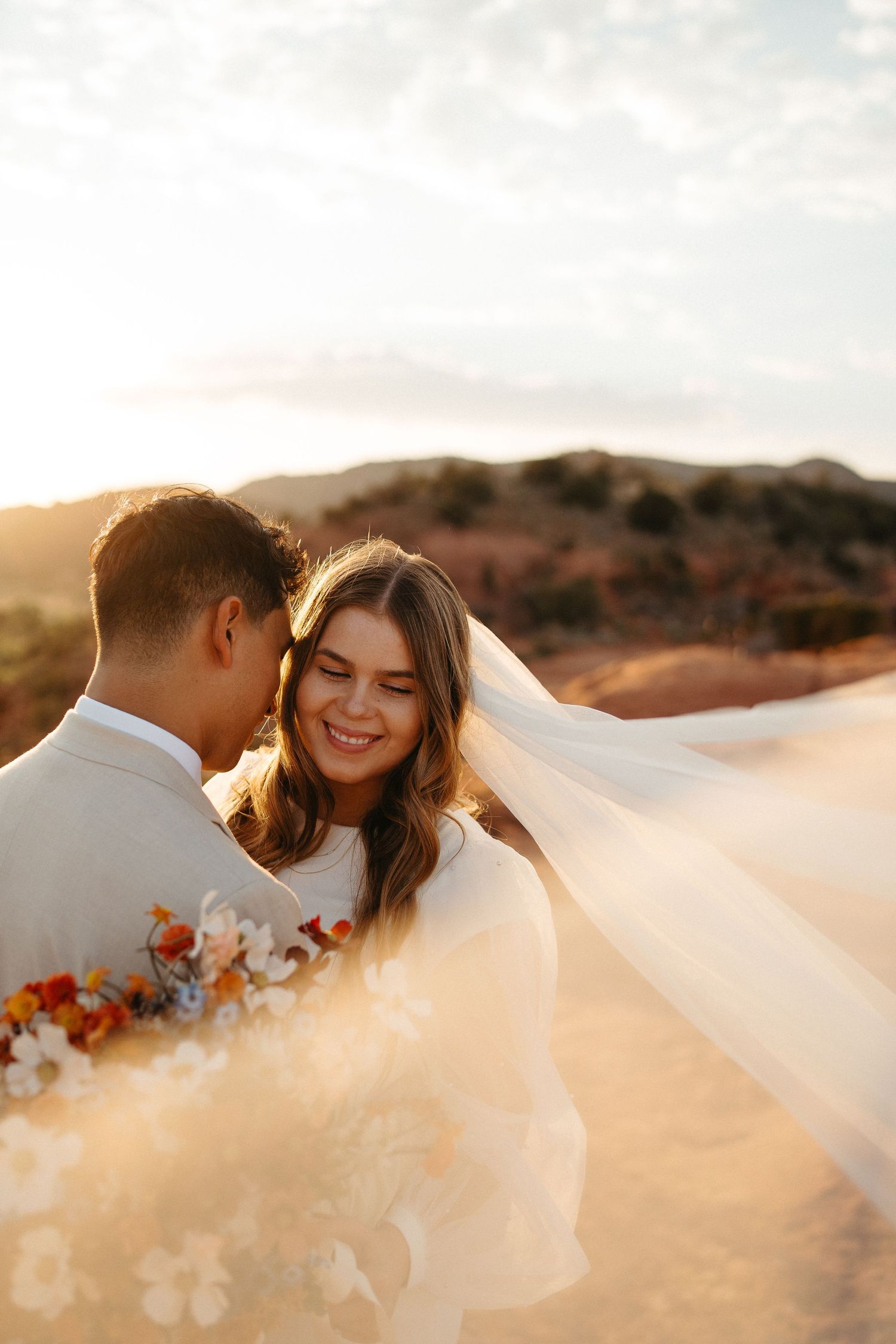 Intimate sunset portrait with flowing veil and autumn bouquet in desert setting.