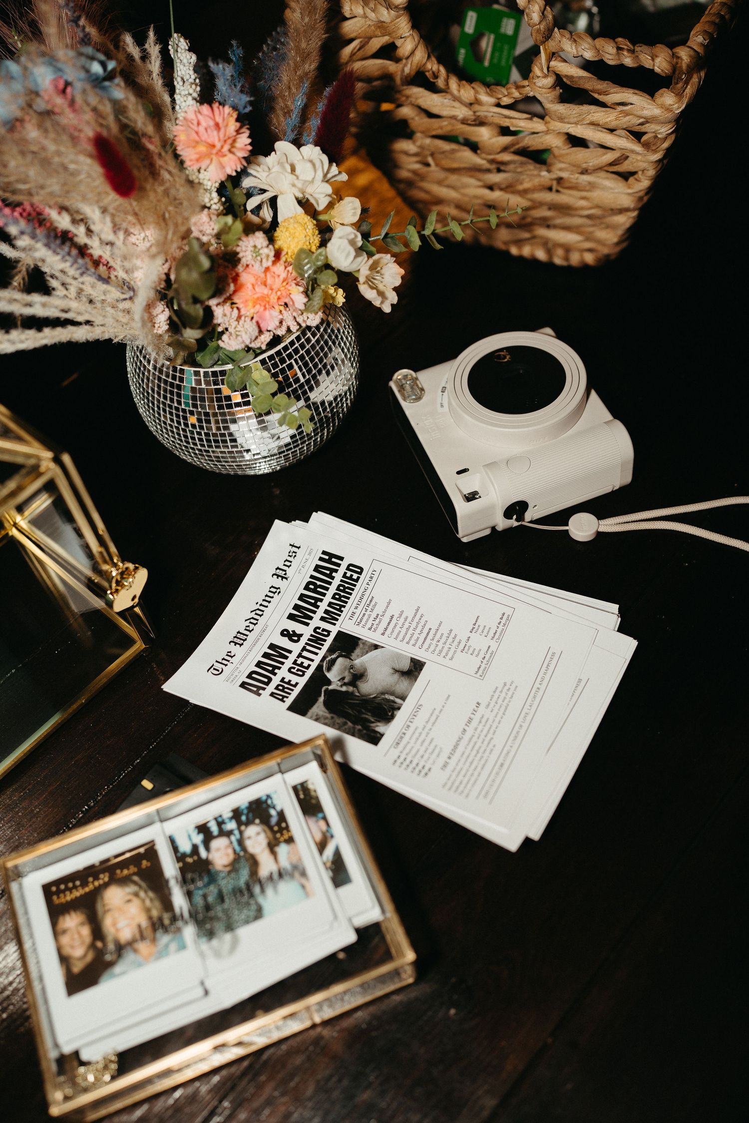 Wedding details including floral arrangements, disco ball decor, and printed documents laid out on a dark wooden surface.