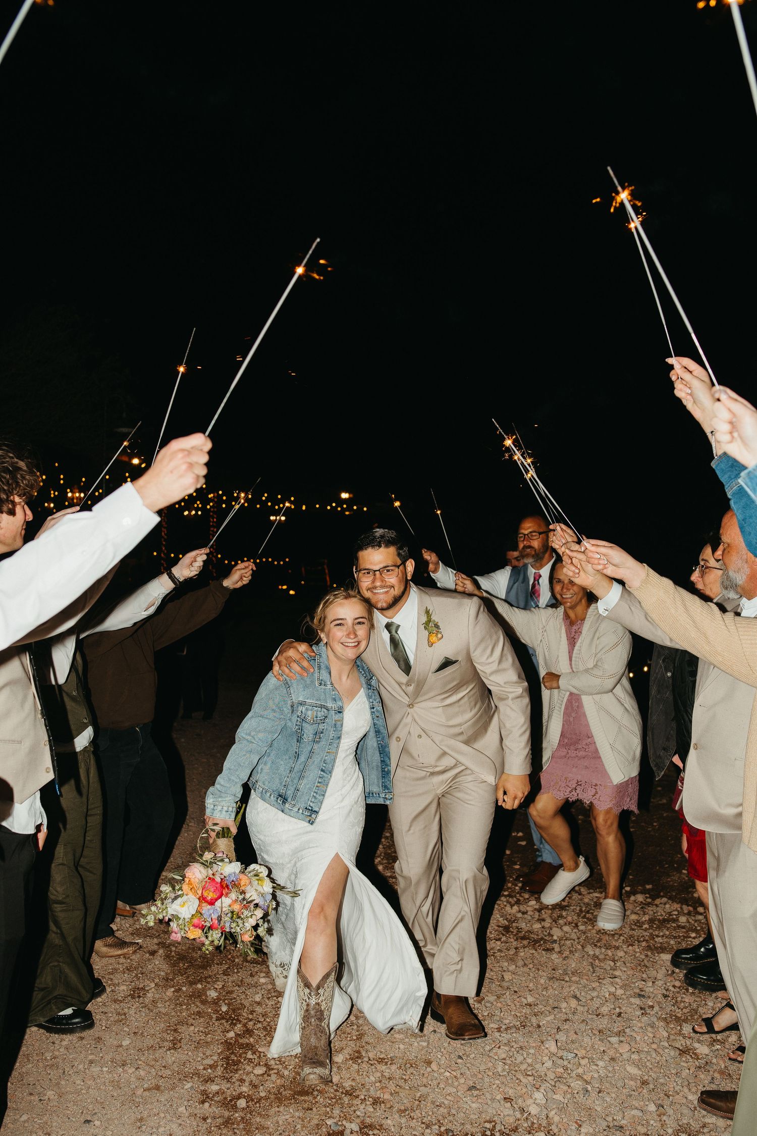 Wedding guests hold sparklers to create a tunnel as a couple exits their reception.