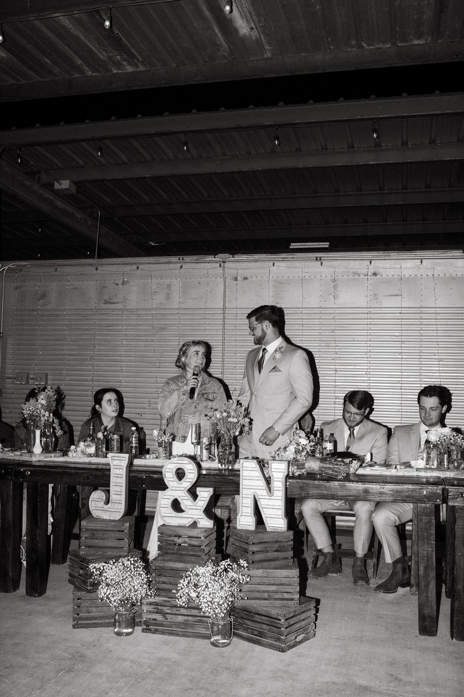 A black and white wedding reception photo with decorative letters J&N displayed on rustic wooden boxes.