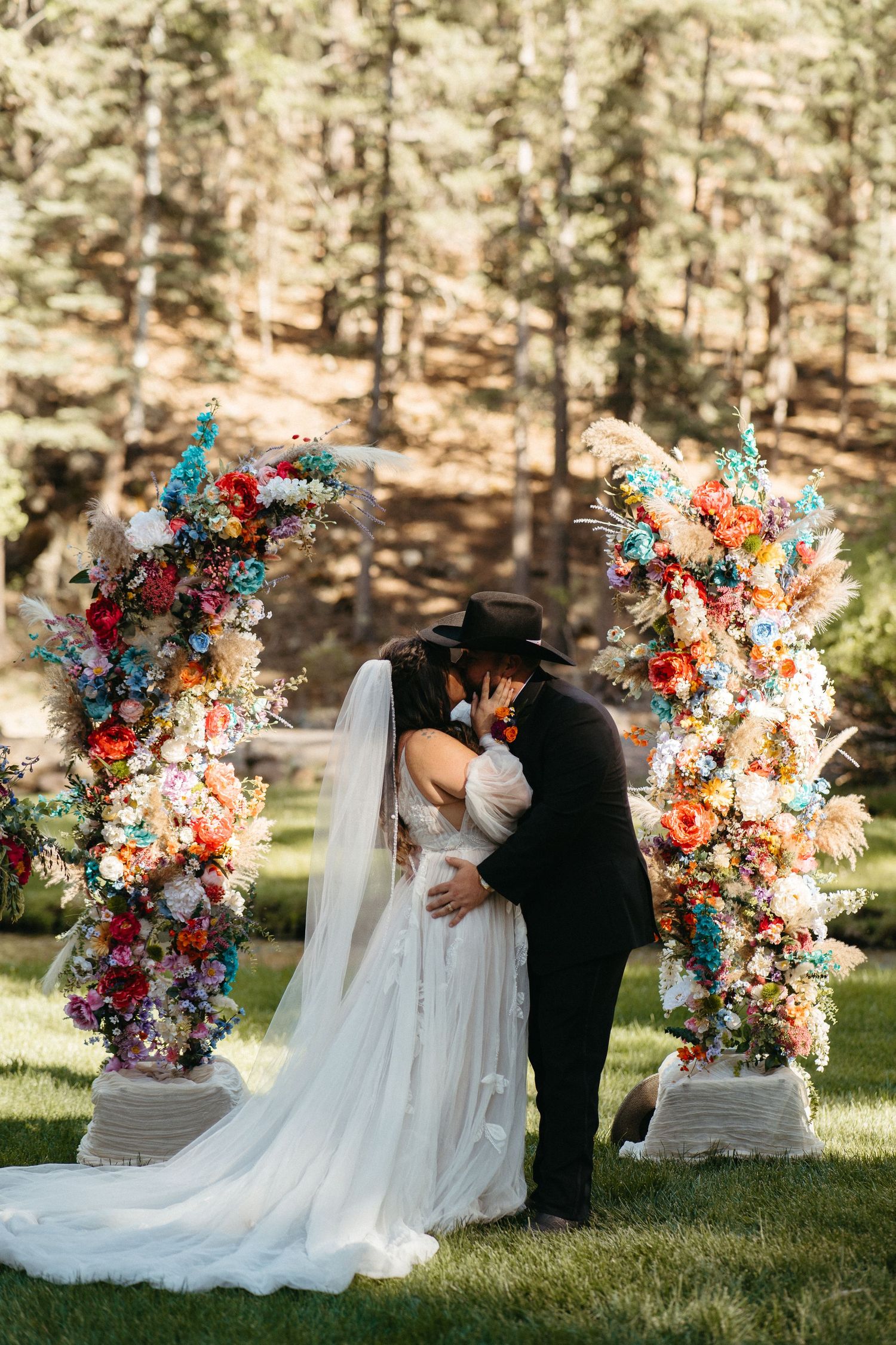 Outdoor wedding ceremony featuring colorful floral arches and decorations in a serene forest setting.