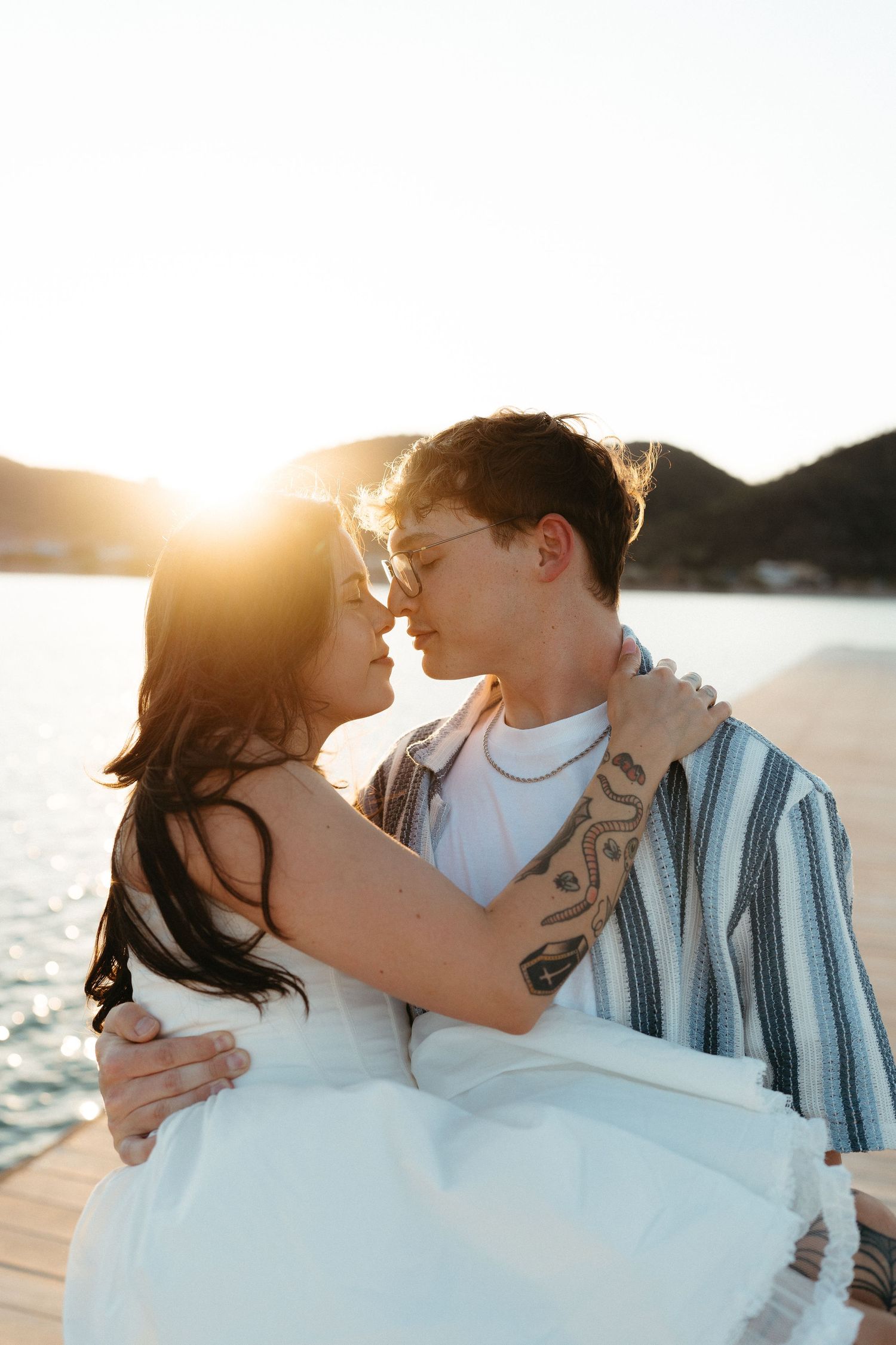 Romantic couple embraces in silhouette against golden sunset light at beach with waves and cliffs in background.