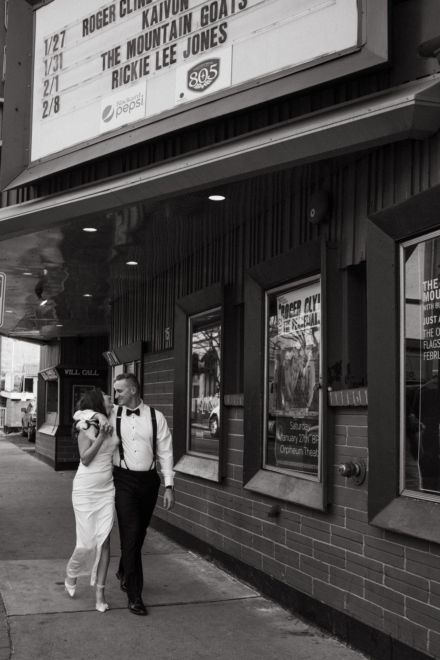 A couple in formal attire walks past a vintage theater marquee.