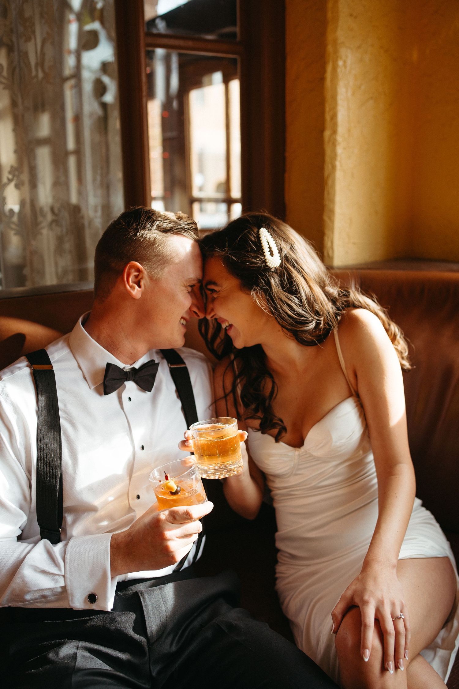 A couple sharing intimate moment with cocktails on leather couch in warm lighting.