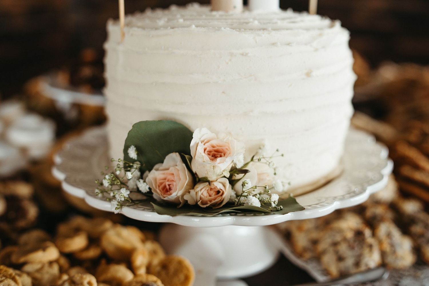 White wedding cake decorated with peach roses and eucalyptus on cake stand.