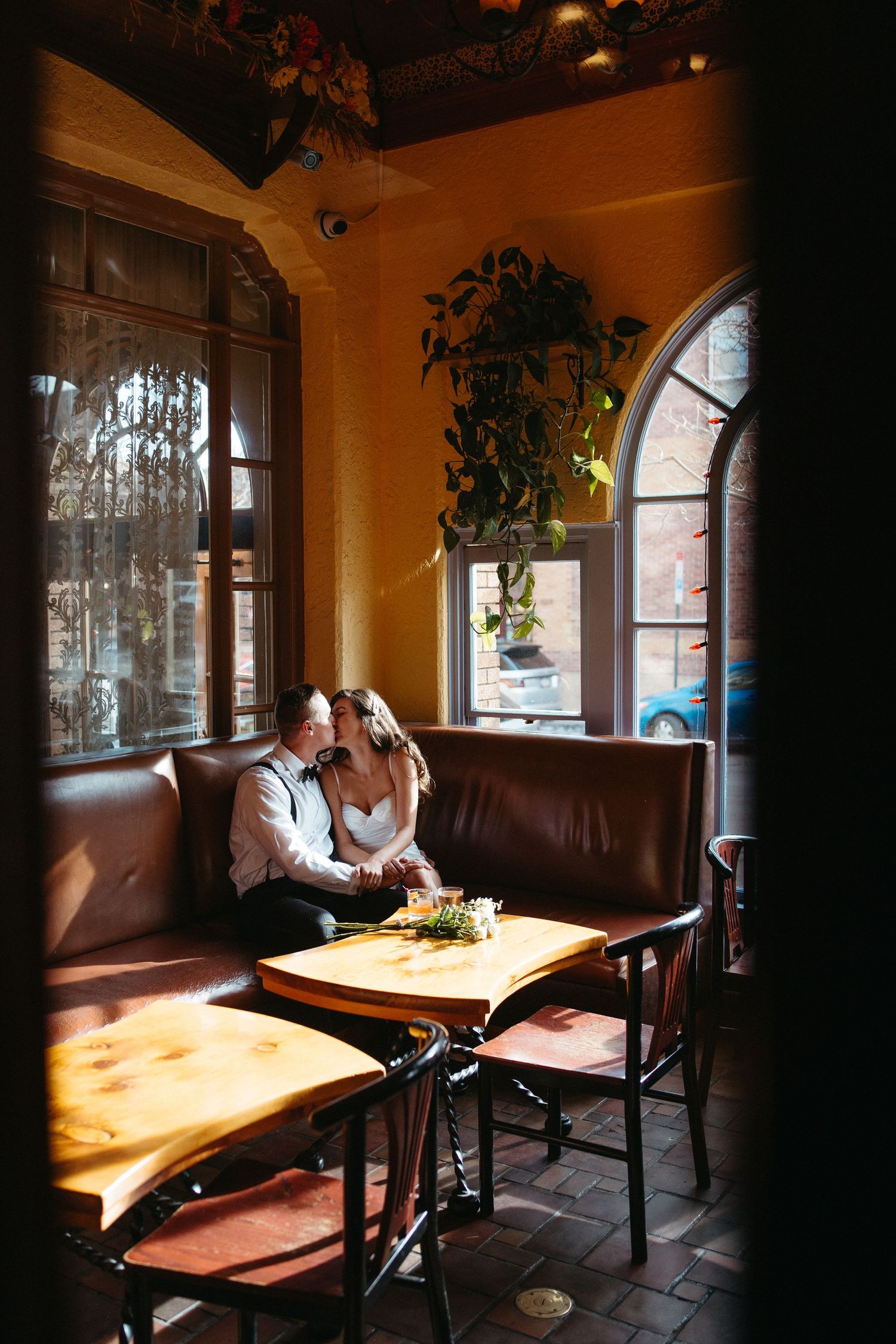 Couple sharing intimate moment in sunlit restaurant booth with arched windows.
