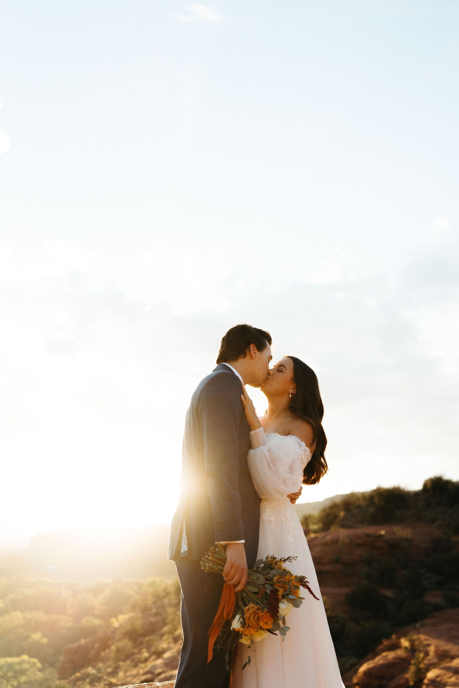Newlywed couple embraces during sunset photo session on mountain ridge with warm golden light.