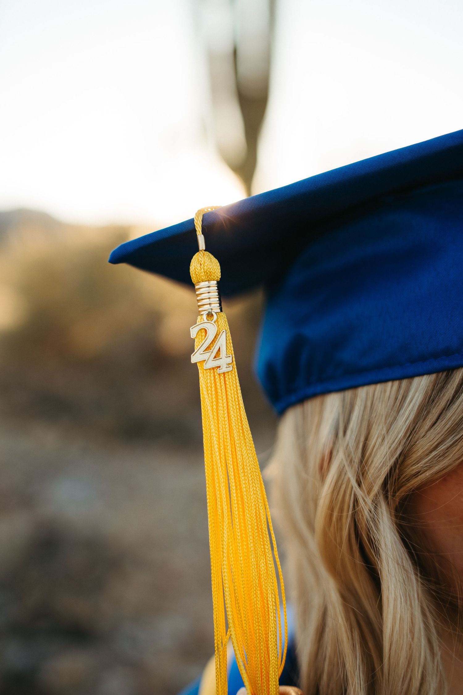 Close-up of yellow graduation tassel against blue cap in desert setting.