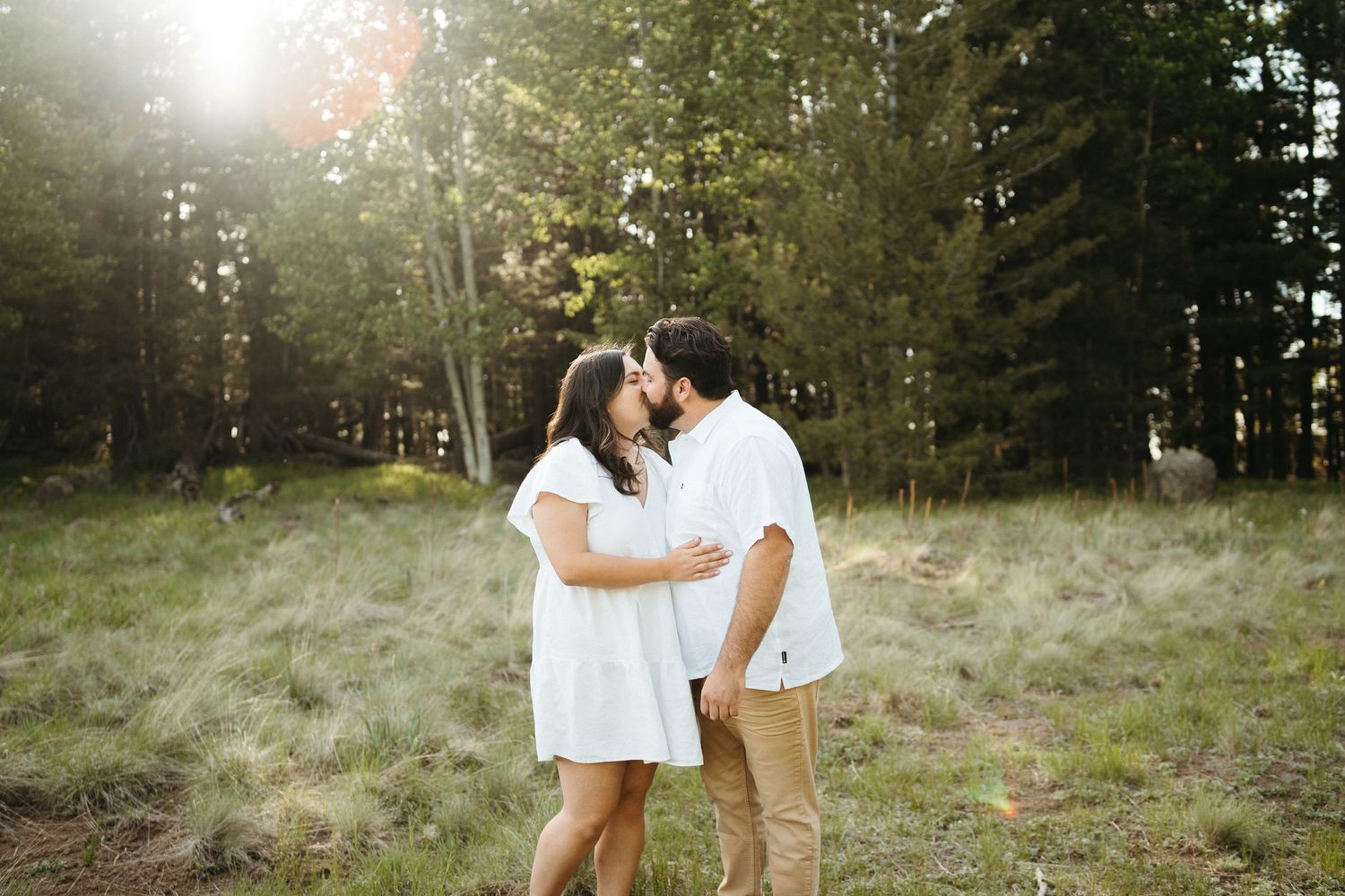 Romantic embrace in a sunlit forest clearing with golden light filtering through trees.