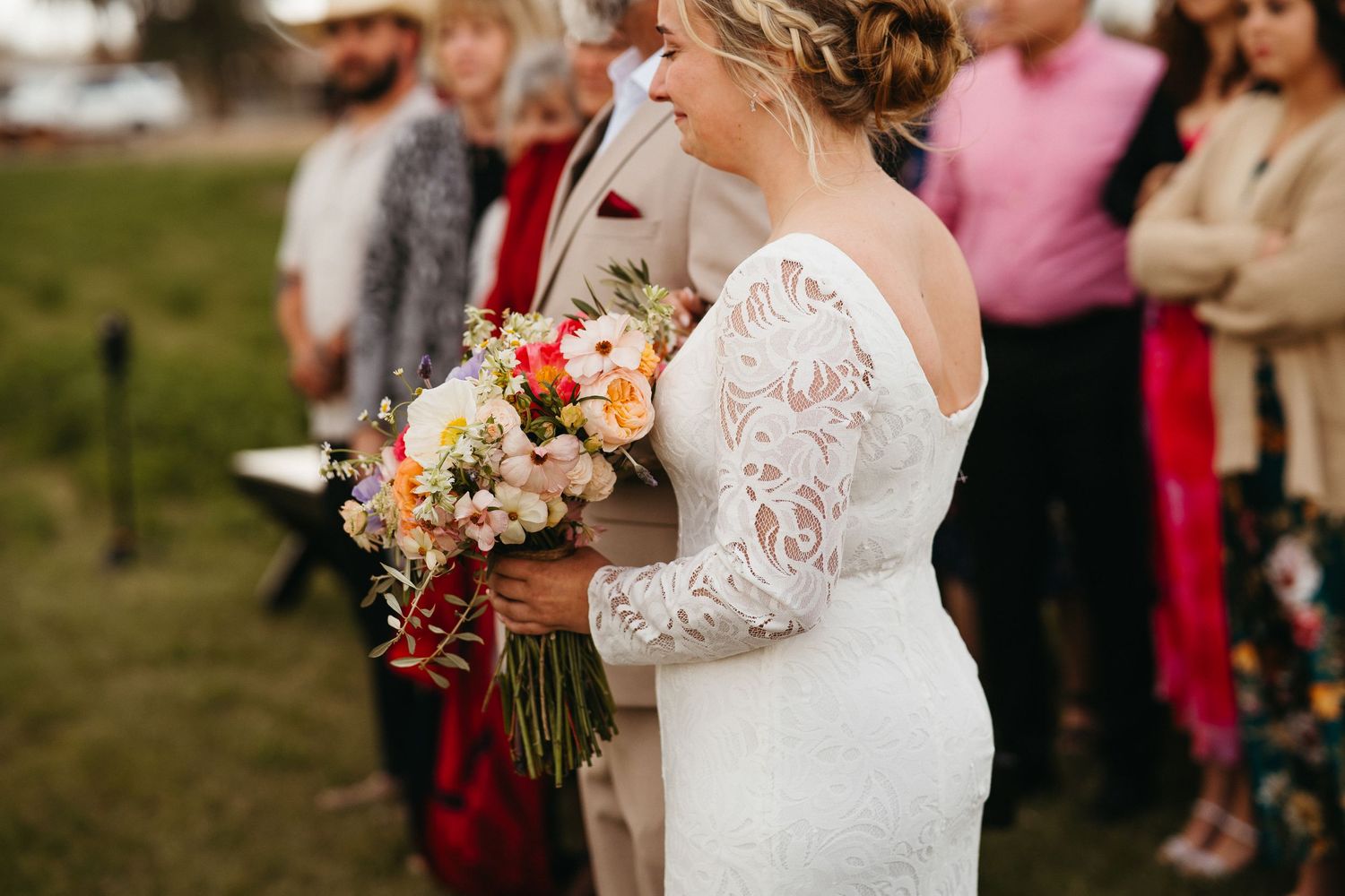 Close-up of bride holding colorful bouquet in lace long sleeve wedding dress.