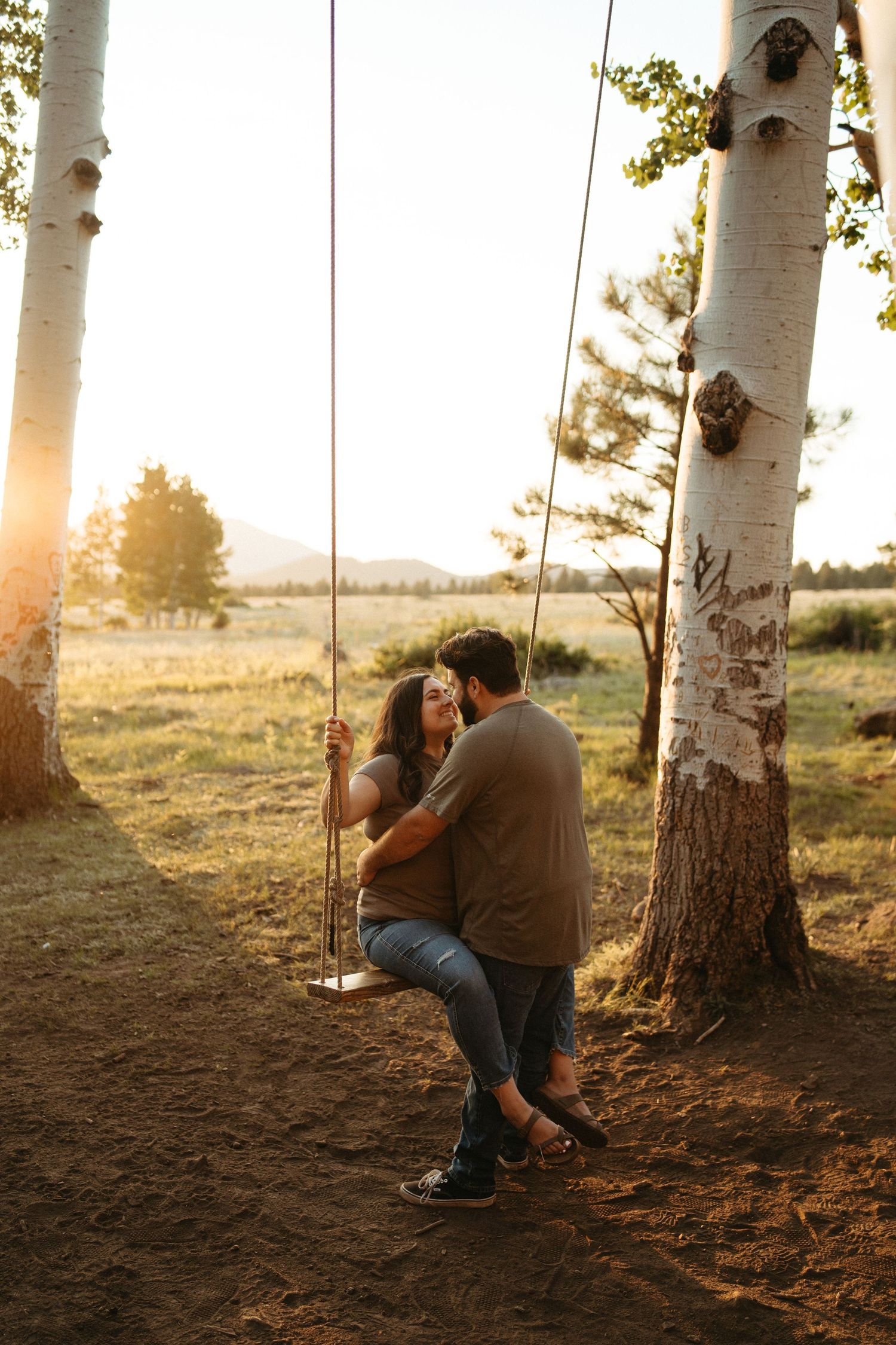 Couple sharing an intimate moment on a tree swing at sunset with aspen trees in the background.
