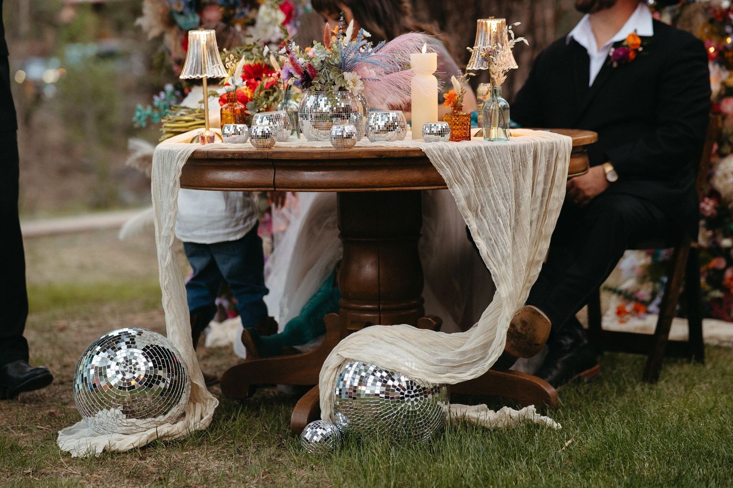 A romantic wedding reception table setting outdoors with flowing white linens and floral arrangements at sunset.