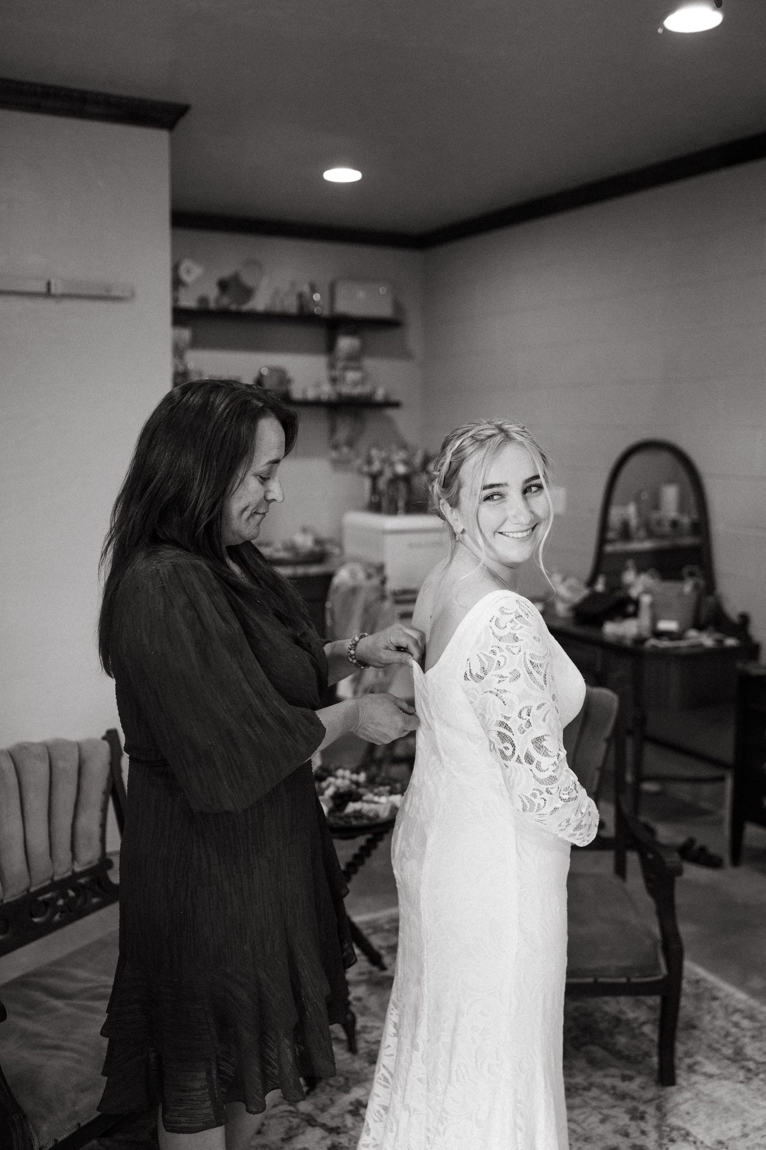 Wedding dress fitting scene in a cozy preparation room with white walls.