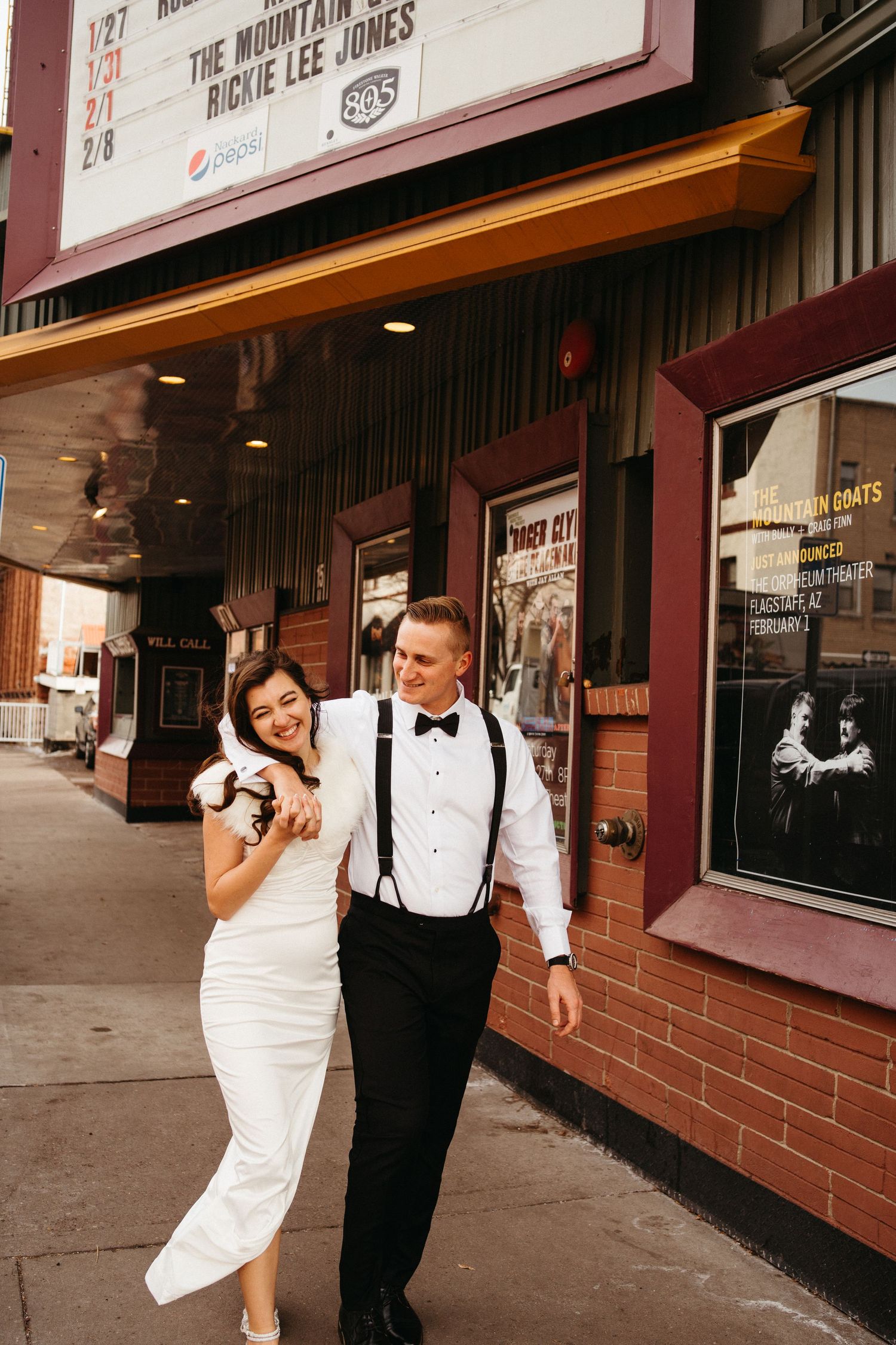 A couple shares a laugh while walking past a movie theater with vintage posters.