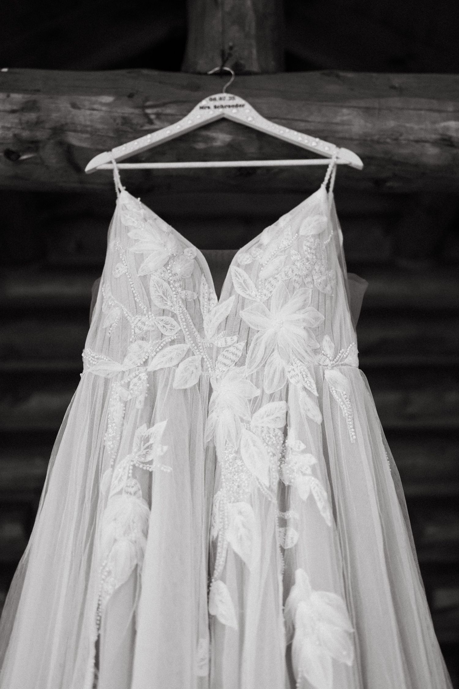 A row of delicate white wedding dresses with lace details hanging on hangers in black and white photography.