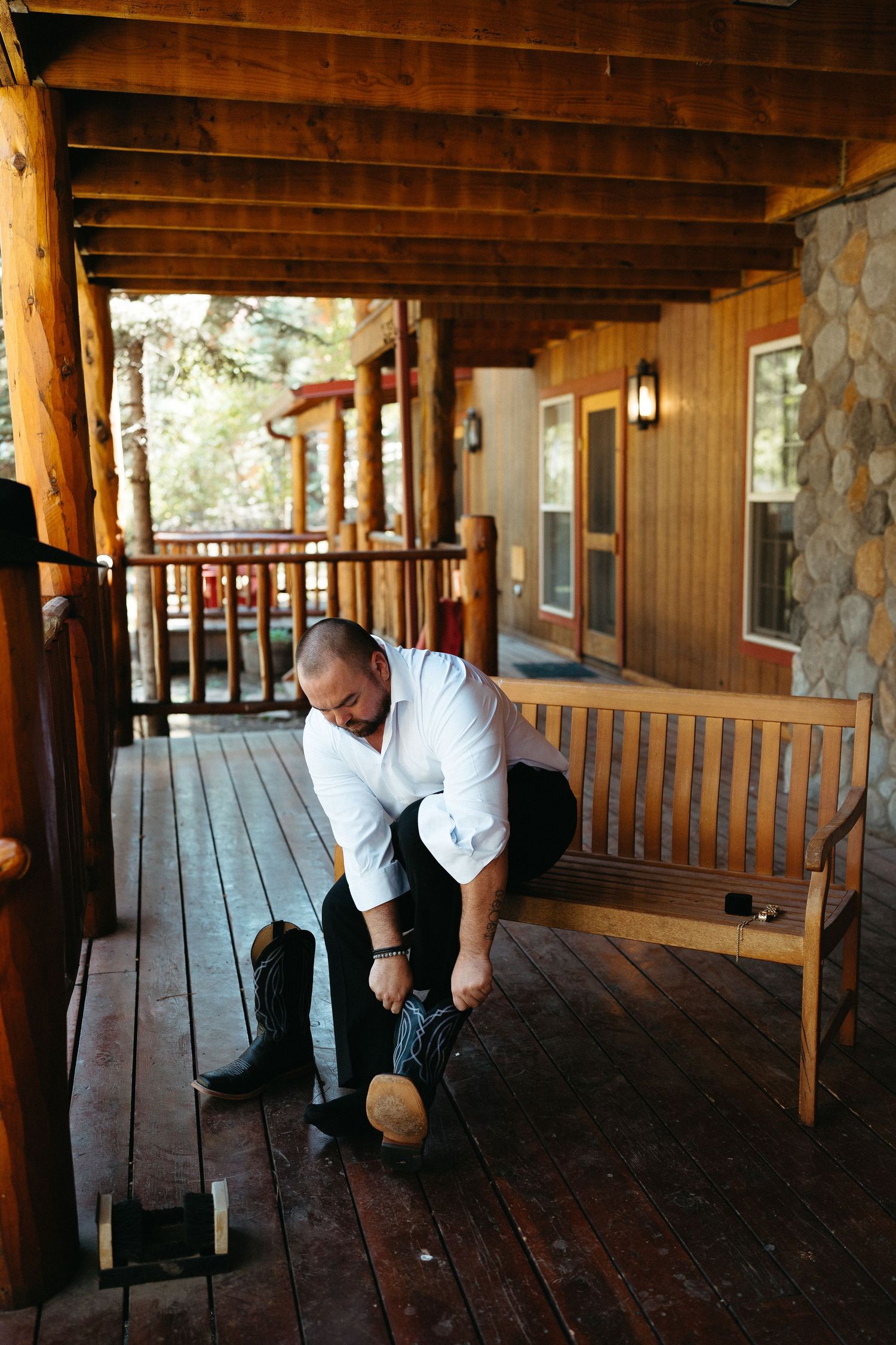 Groomsmen prepare for a wedding ceremony on a rustic wooden porch of a mountain lodge.