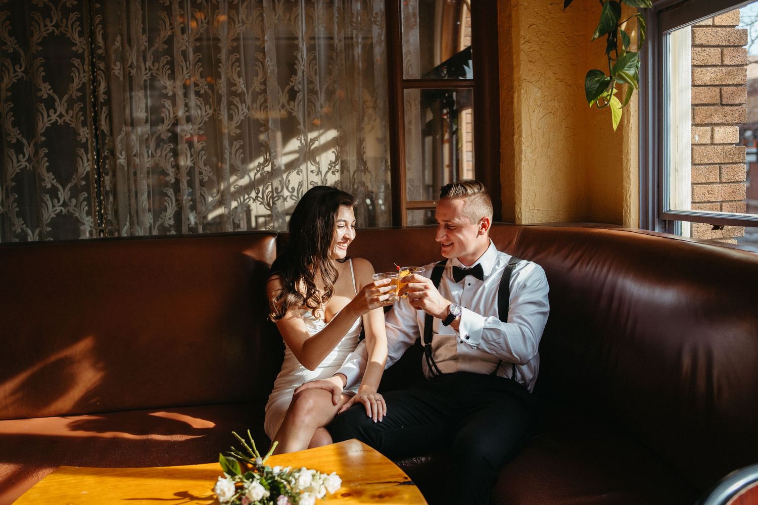 A couple sharing drinks at rustic wooden table with sunlight streaming through window.