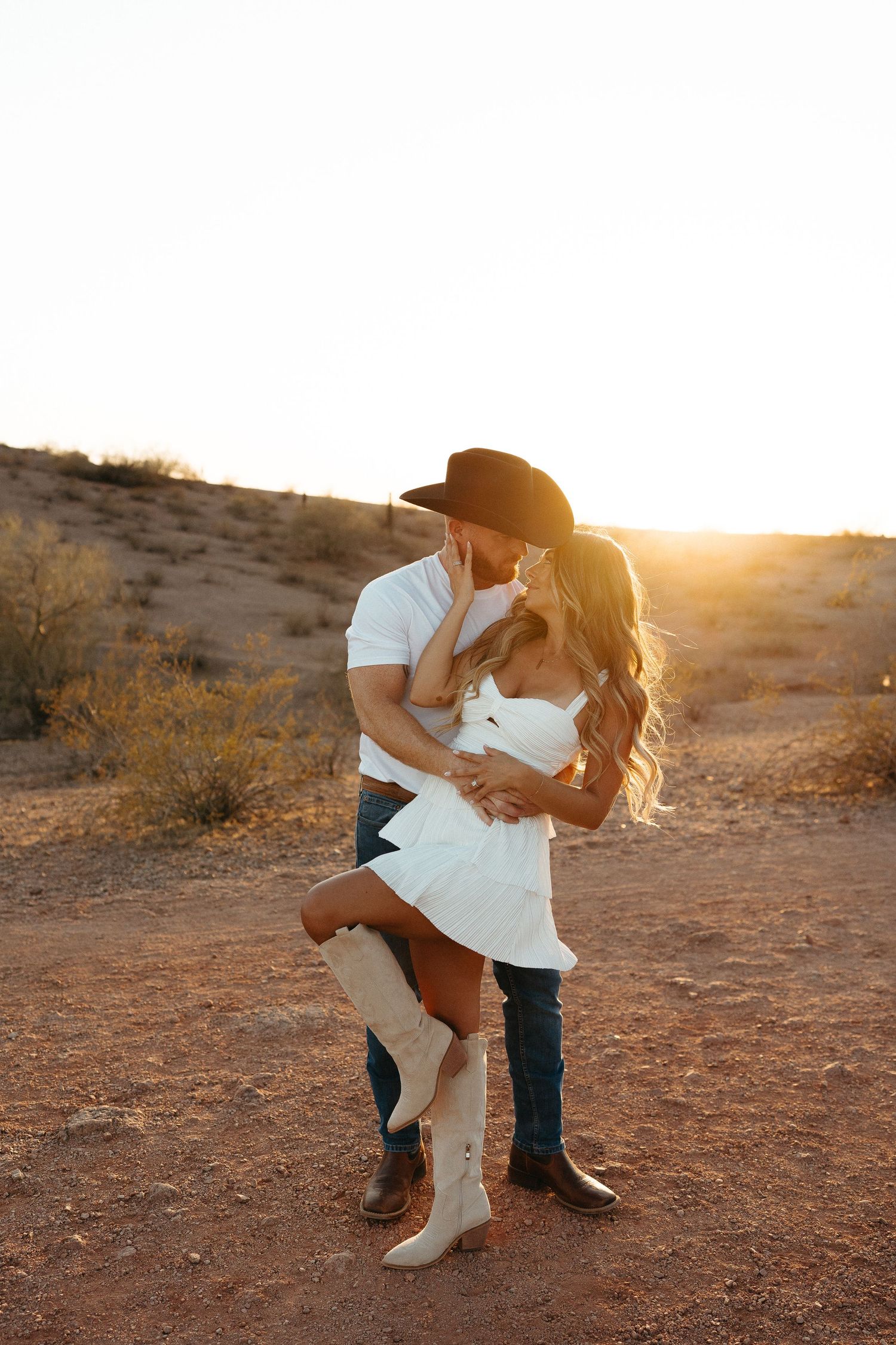 Dancing couple shares intimate moment in desert setting with dramatic sunlit mountain backdrop.