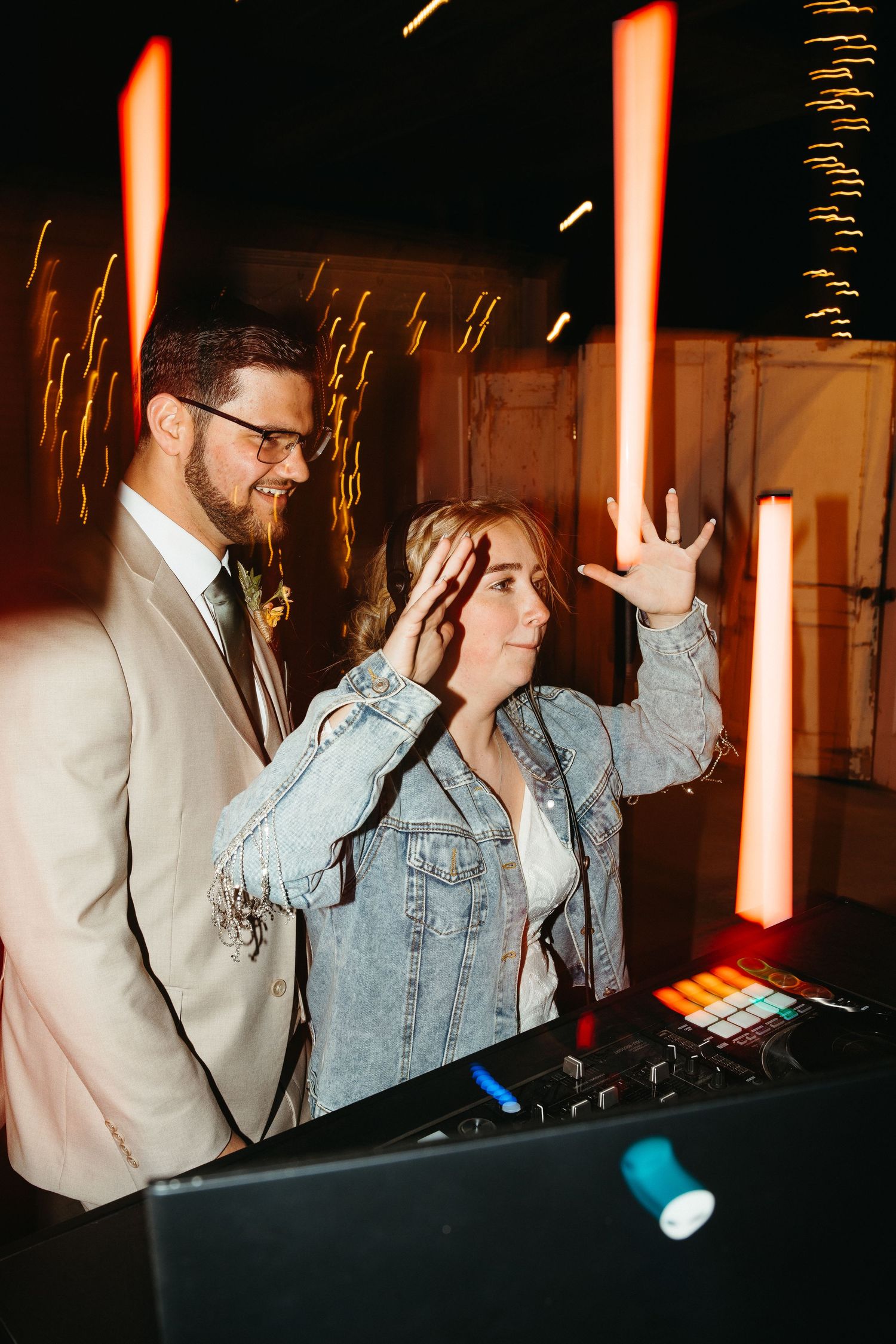 A couple at a DJ booth during their wedding reception with dramatic lighting effects.