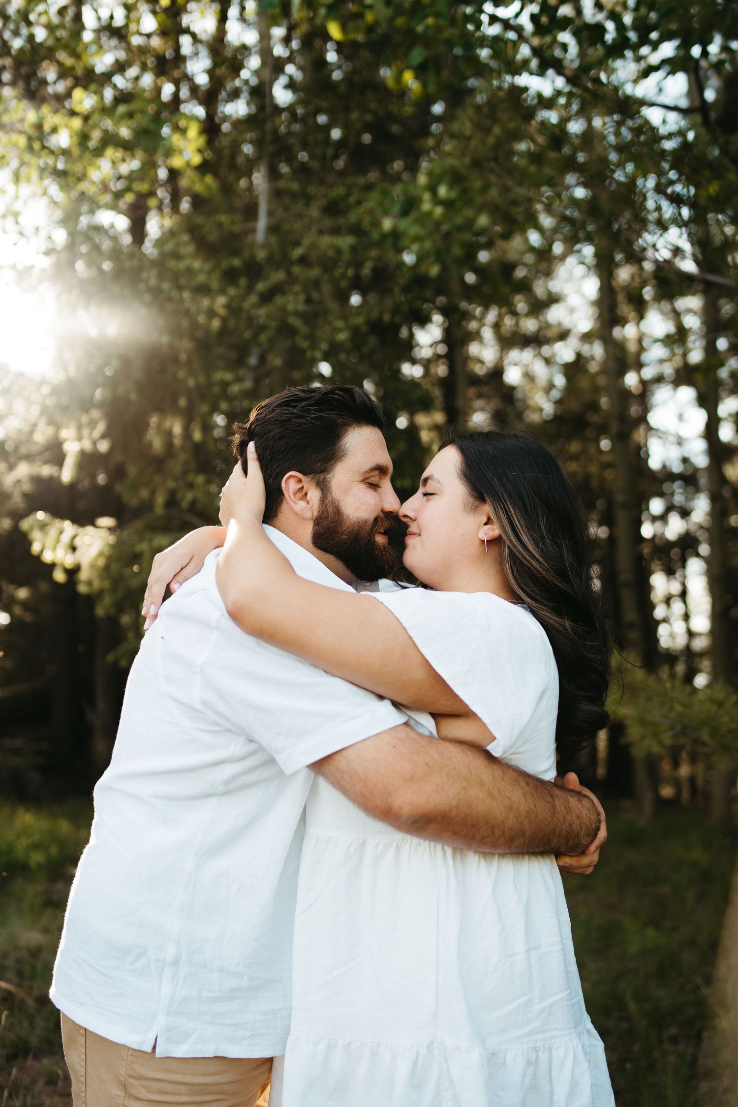 Tender embrace captured in golden sunlight with forest backdrop.