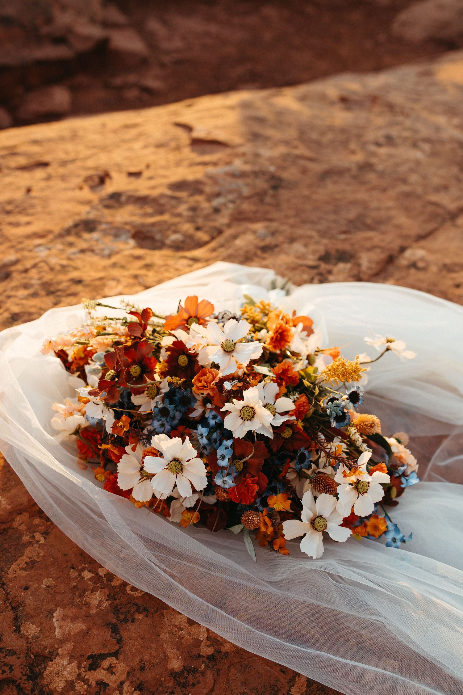 Colorful autumn wedding bouquet with white flowers resting on red rock formation.