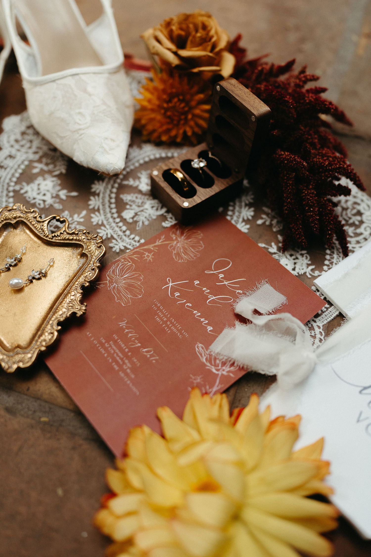 Wedding invitation details with rustic brown cards, white lace doilies, and yellow and burgundy floral accents on wooden surface.