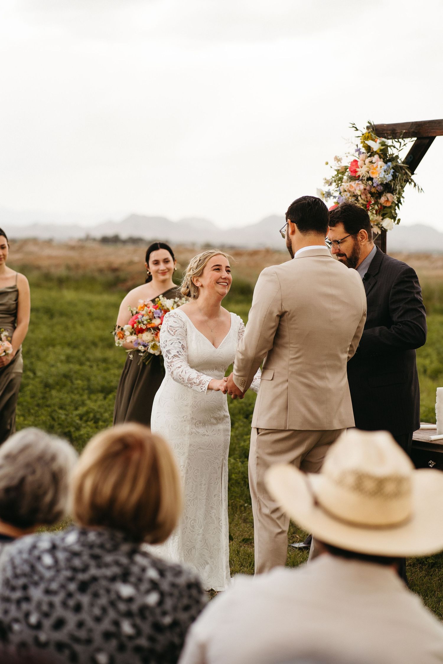 Couple exchanges vows under floral arch during outdoor countryside wedding ceremony.