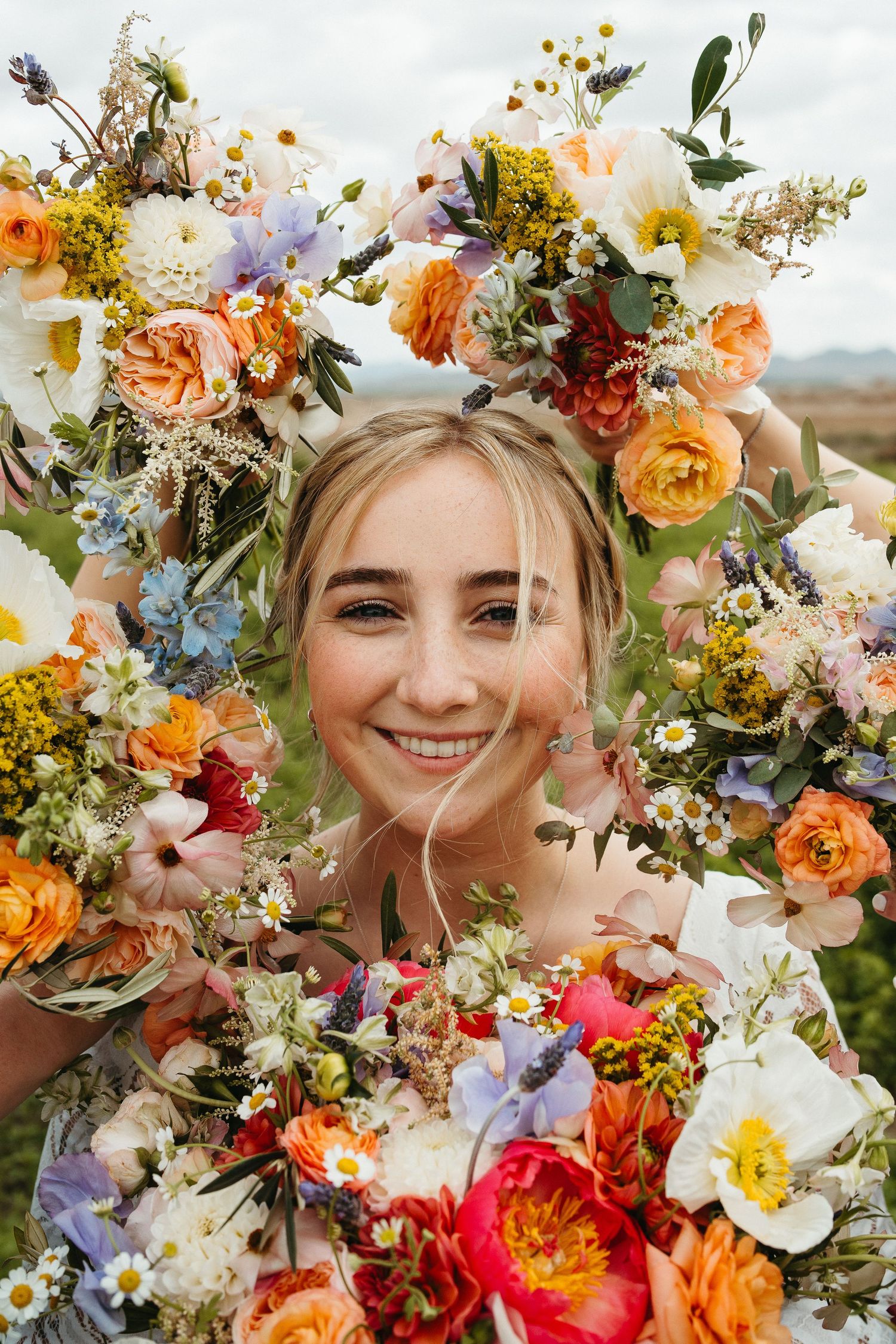Vibrant floral crown with orange, yellow and blue blooms surrounds a joyful close-up portrait.