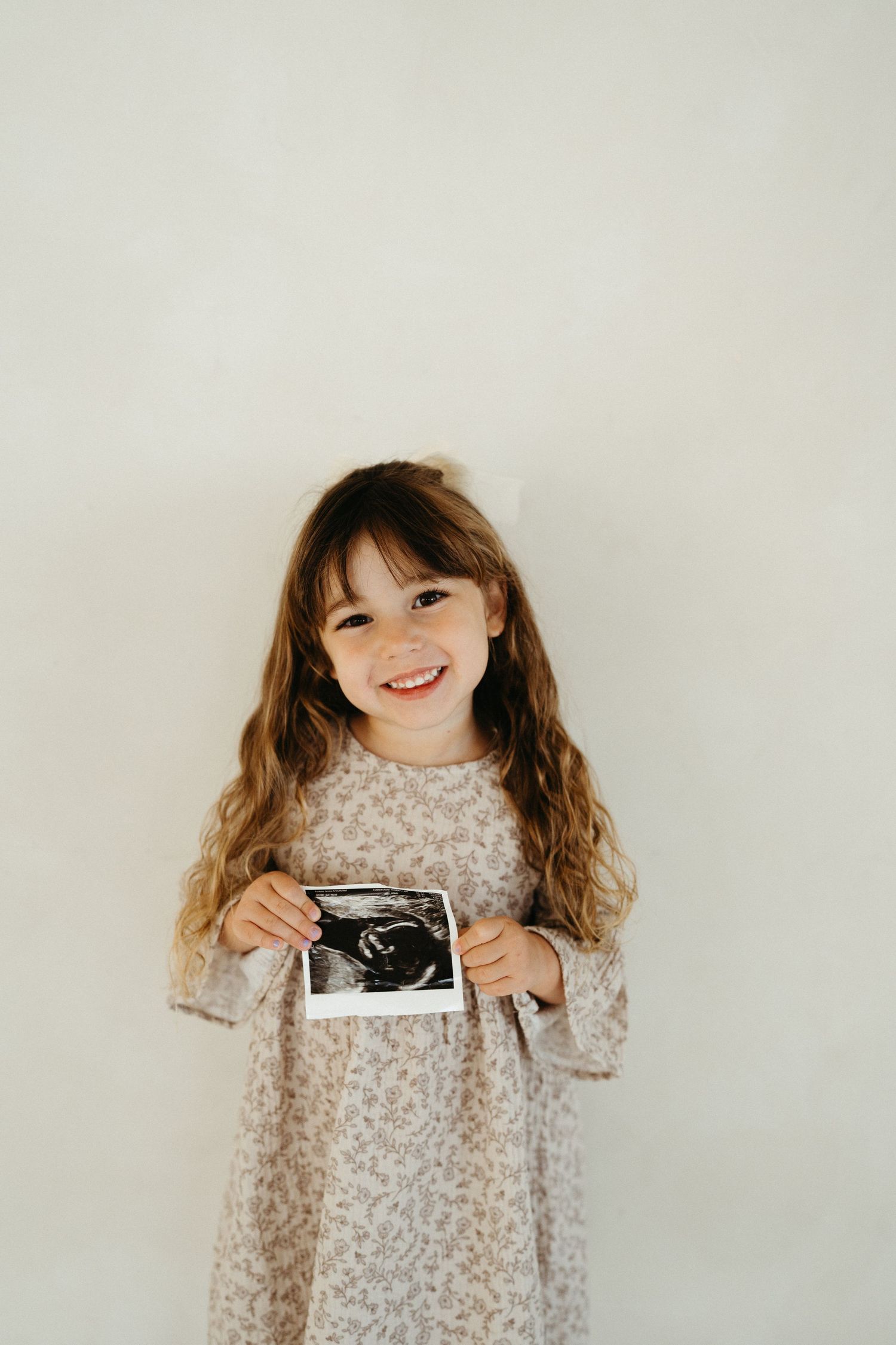 A young child in a floral dress holds a vintage camera against a white background in a series of candid poses.