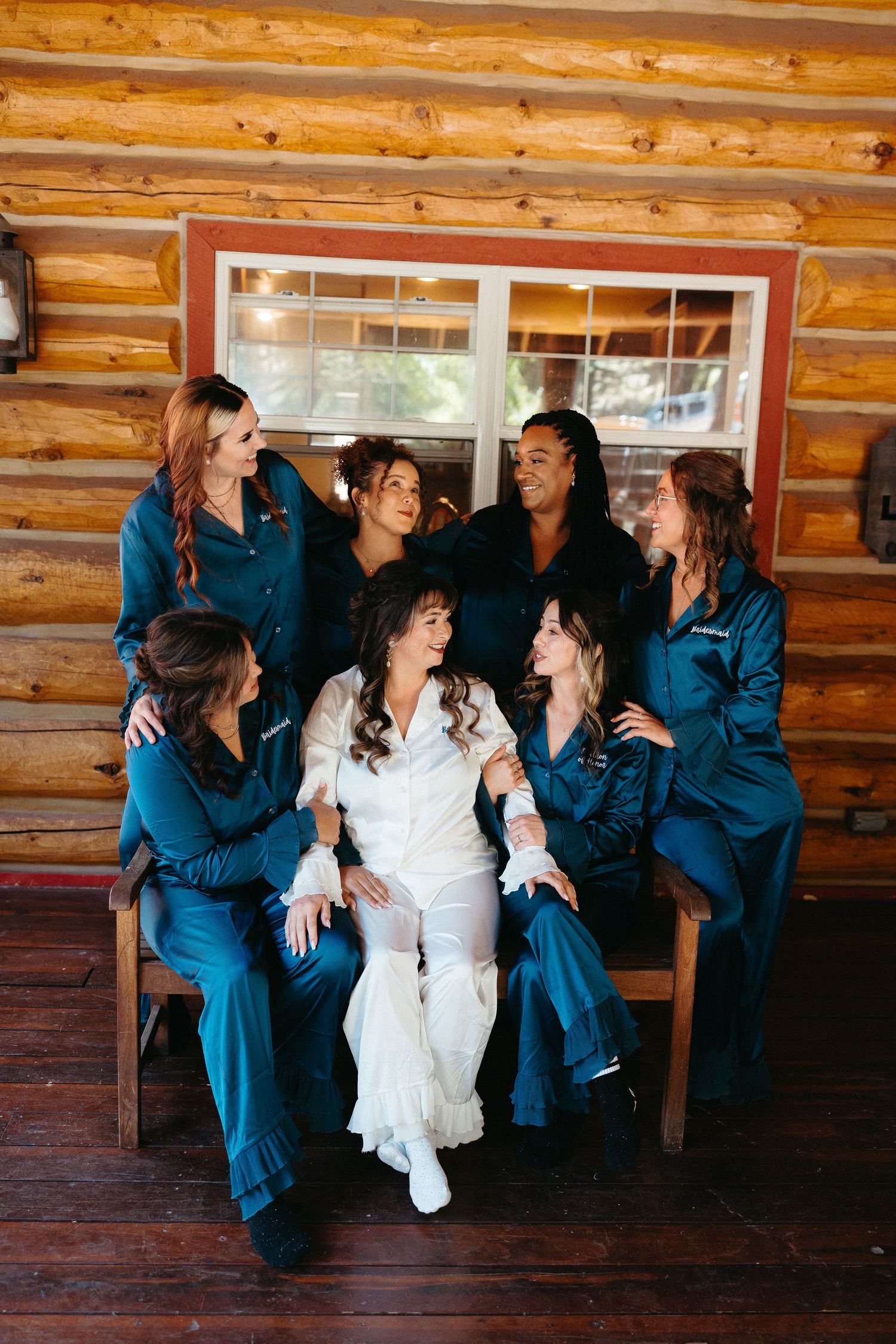 Group wearing matching denim outfits gather around someone in white dress on rustic wooden porch.