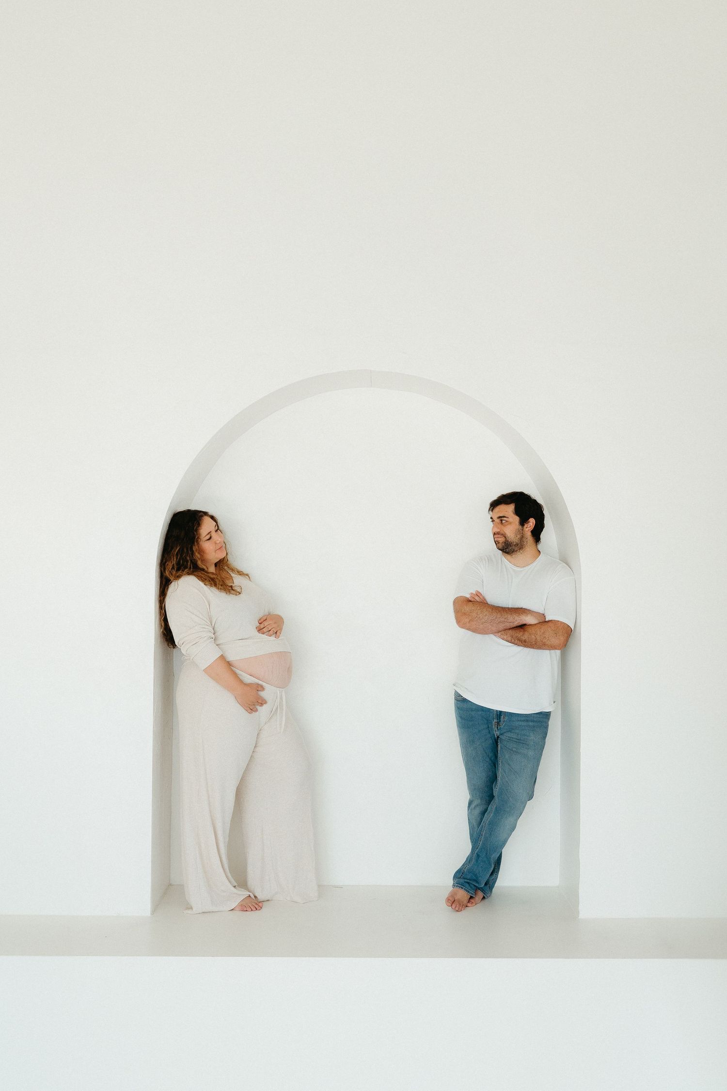 Two people creatively positioned in minimalist white arched doorways creating an artistic composition.