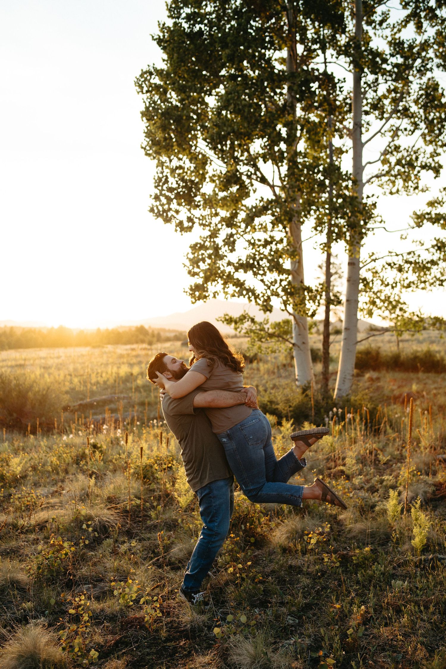 A joyful couple embracing and spinning in a field during golden hour with aspen trees nearby.