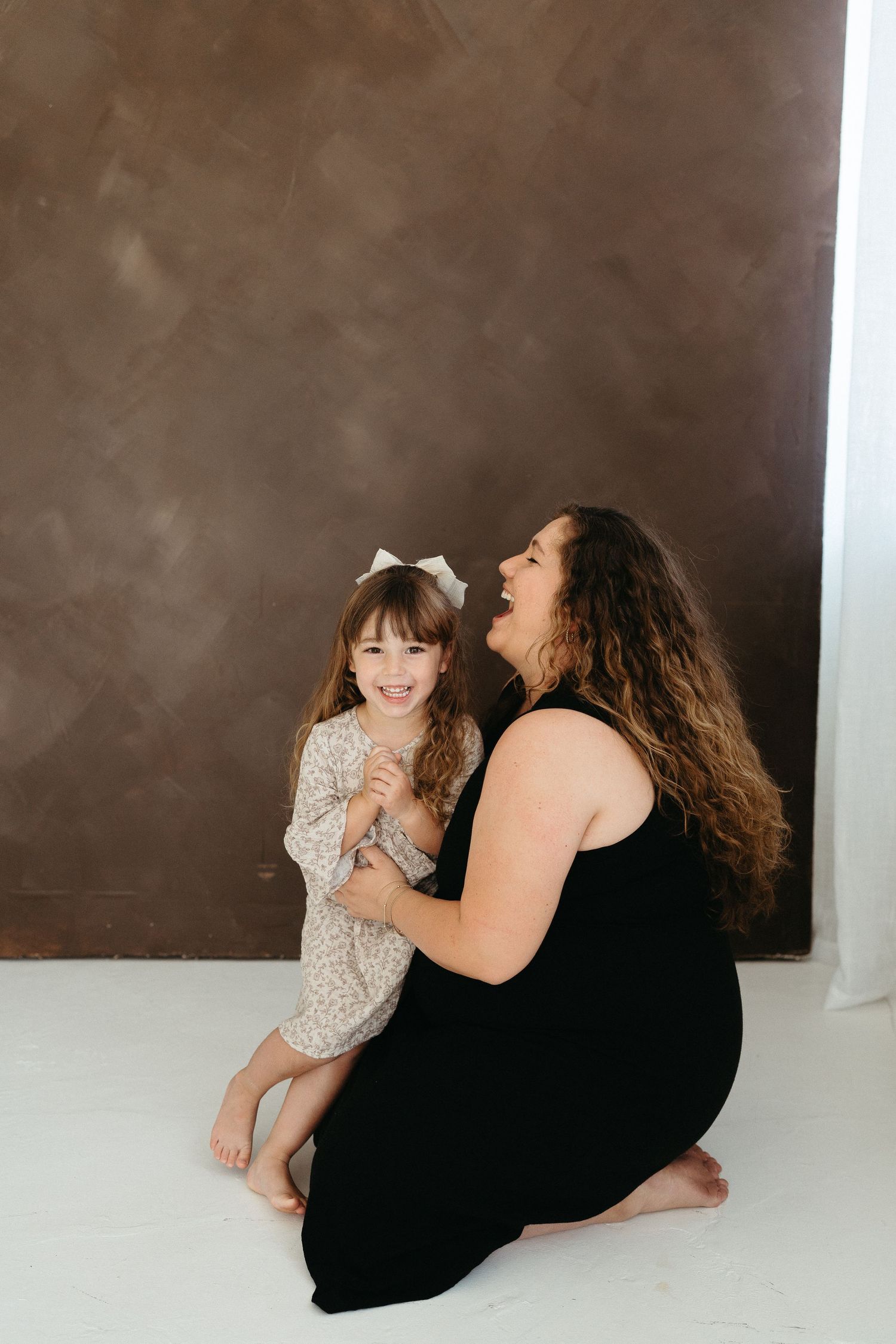 Candid studio portrait of two people laughing and bonding together against brown backdrop.