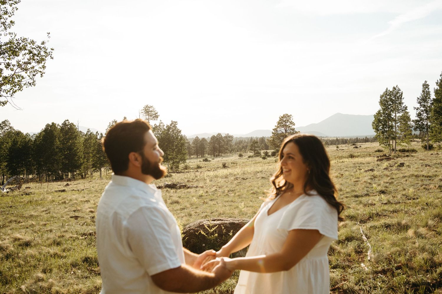 A couple sharing a joyful moment while dancing together in a grassy field at sunset.