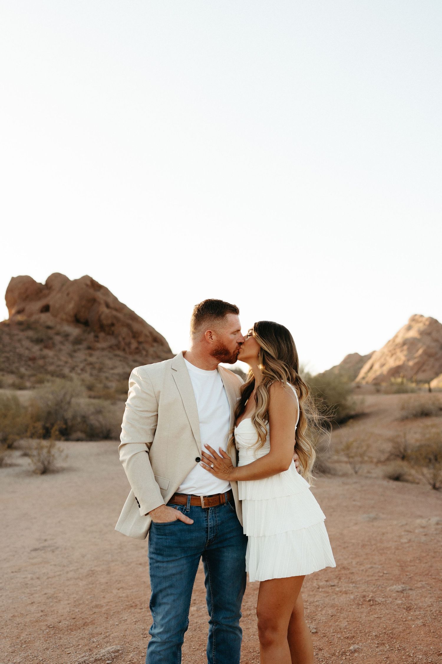 Romantic couple embraces against desert rock formations during golden hour photoshoot in the American Southwest.