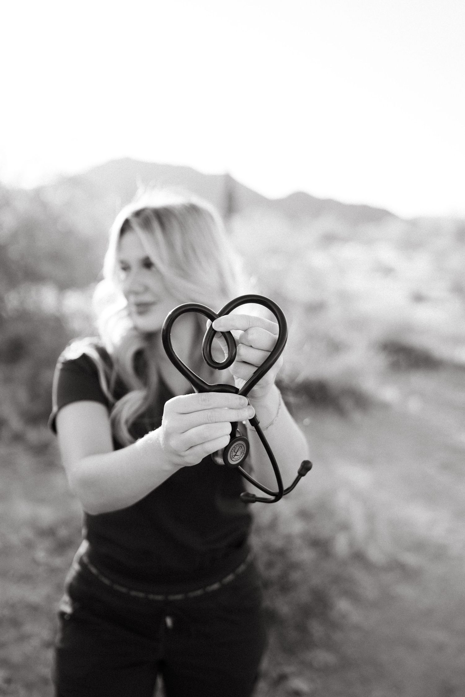 Person holding heart-shaped prop against desert mountain backdrop in monochrome.